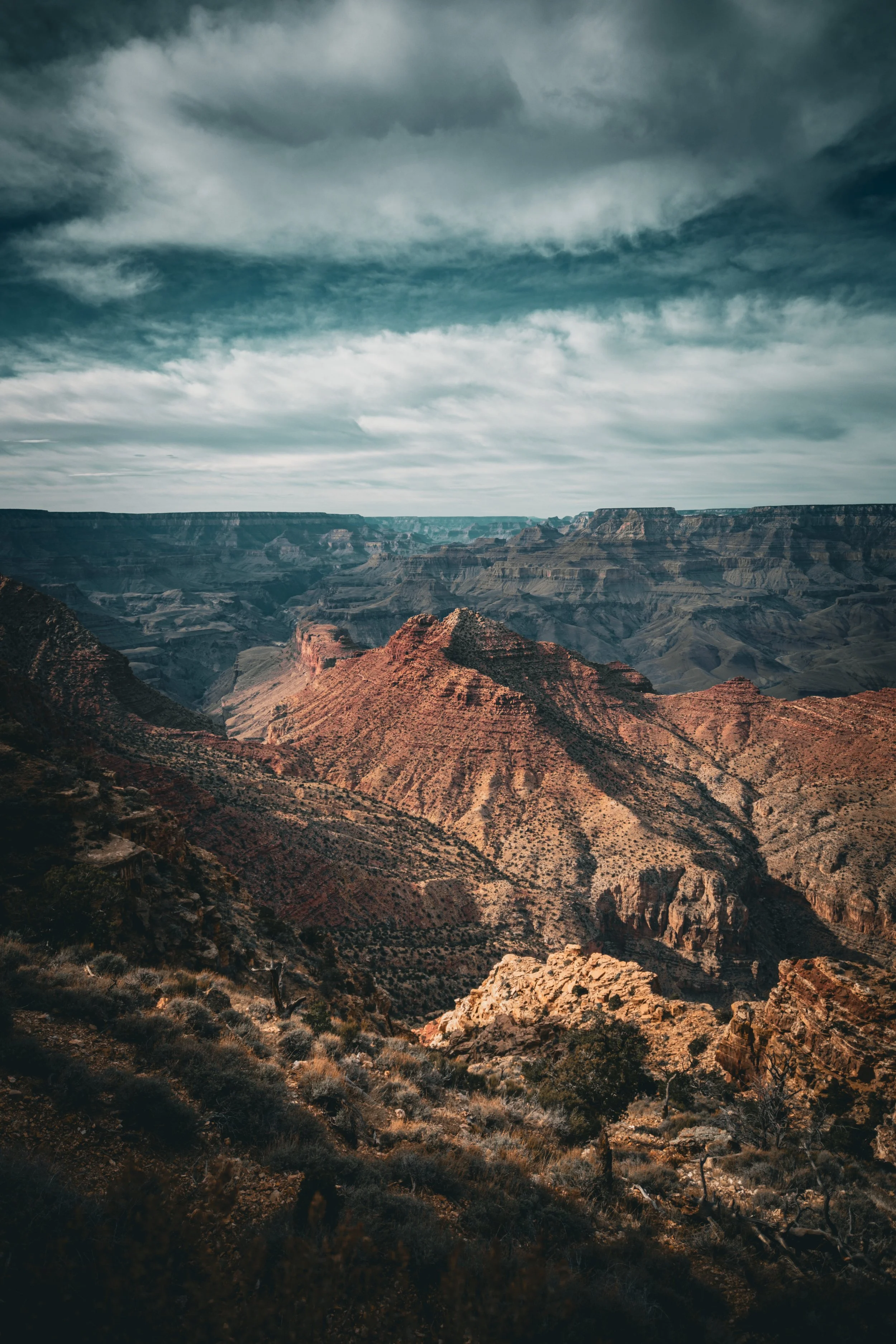 View of the Grand Canyon with layered rock formations and dramatic clouds overhead.