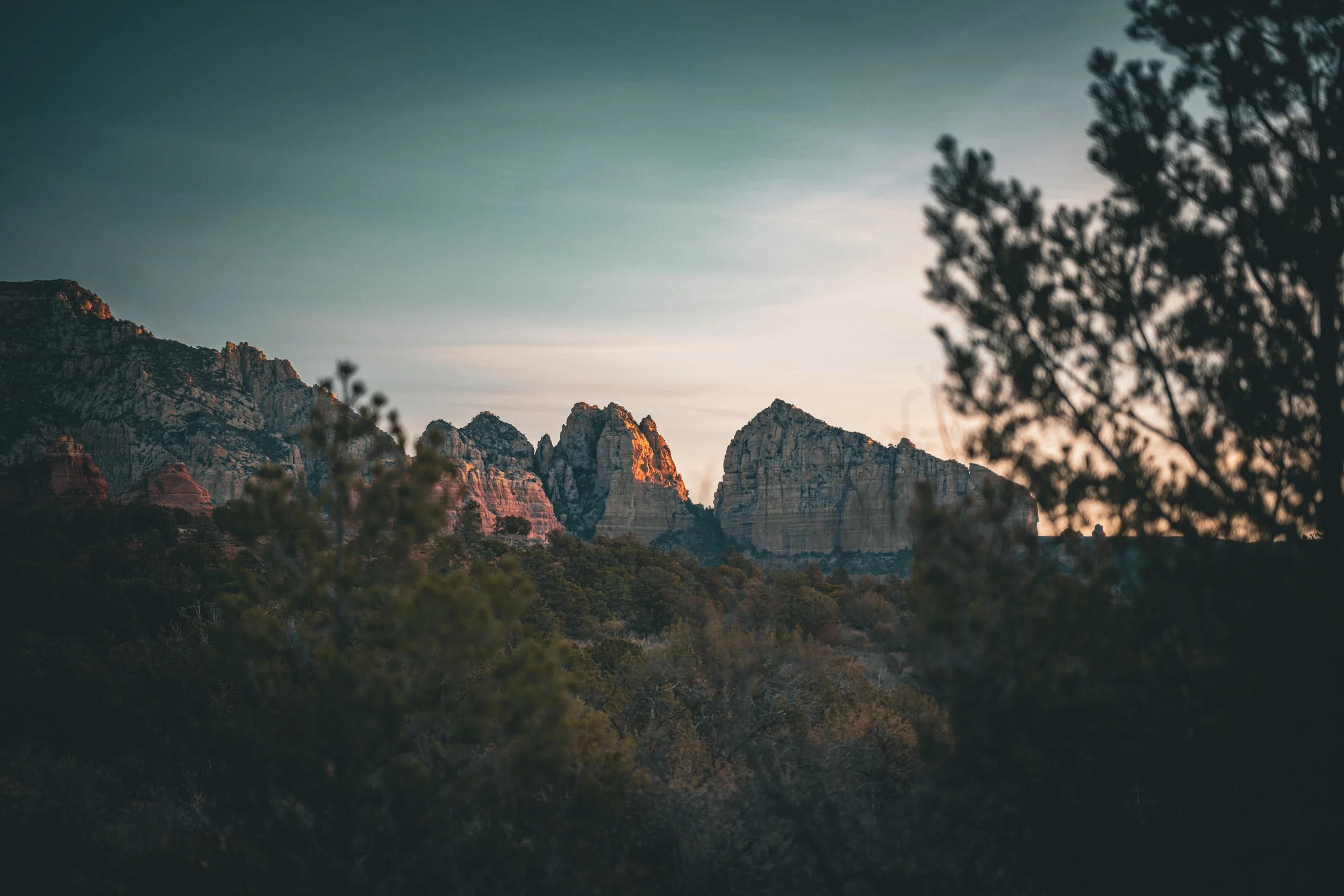 Sunset over rocky mountain range with trees in foreground.