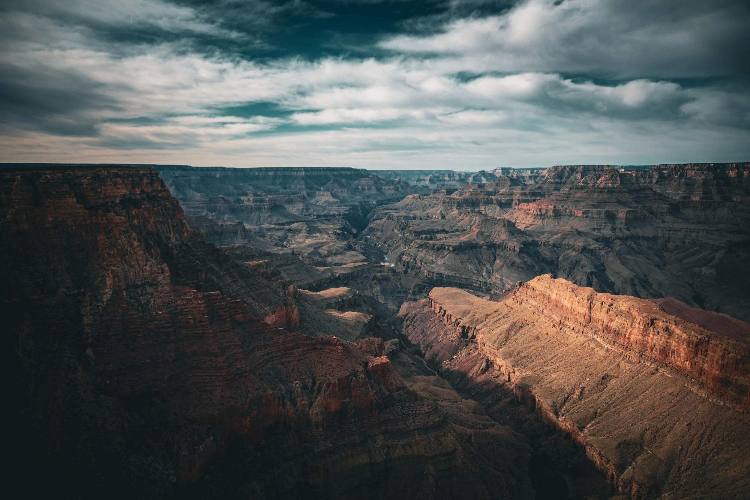 View of the Grand Canyon with layered rock formations and a cloudy sky overhead.