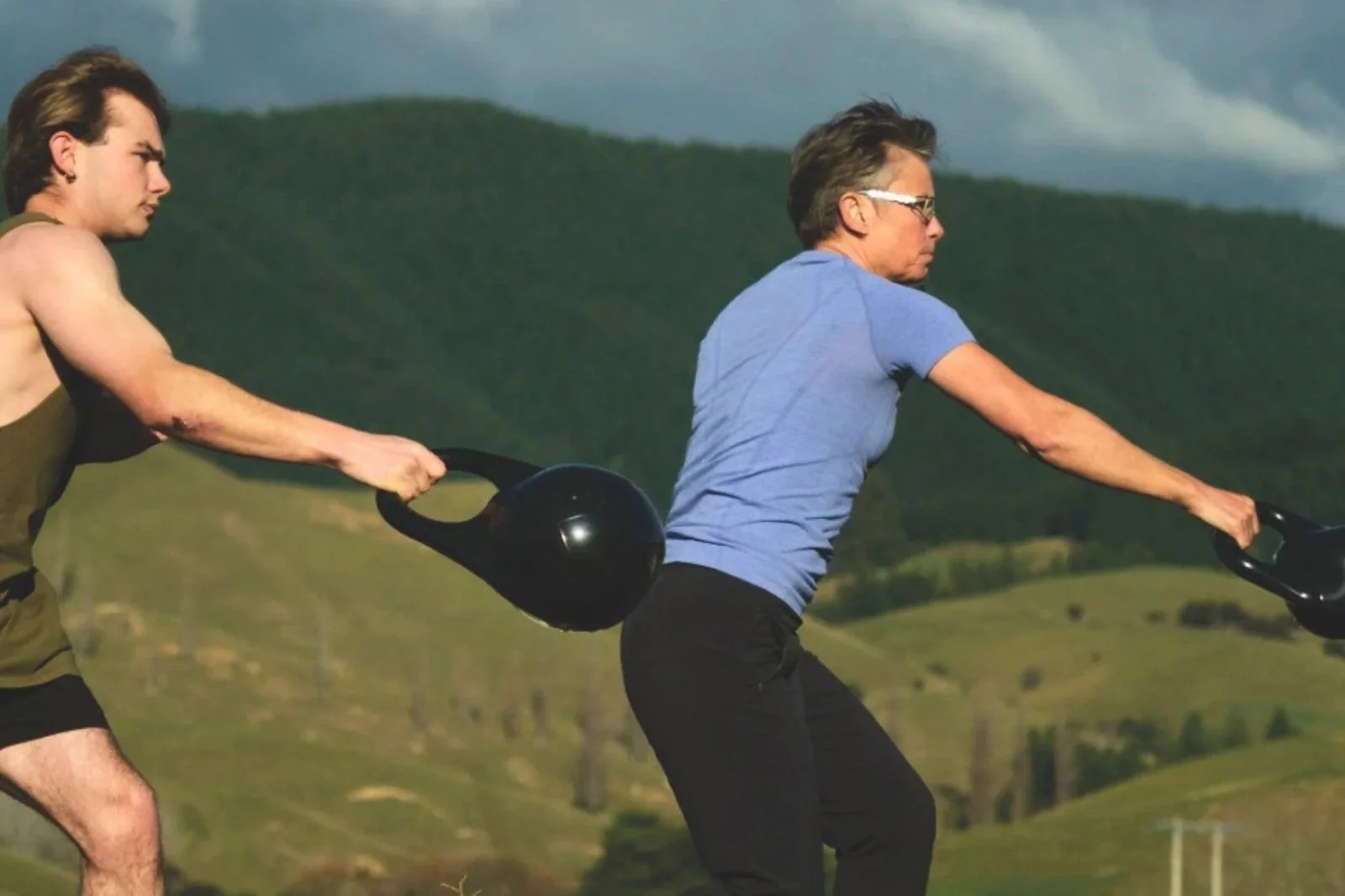 Two people performing kettlebell exercises outdoors.