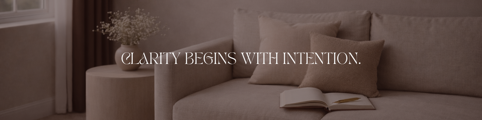 Living room with beige sofa, open book, and decorative pillows, with a vase of flowers on a side table.