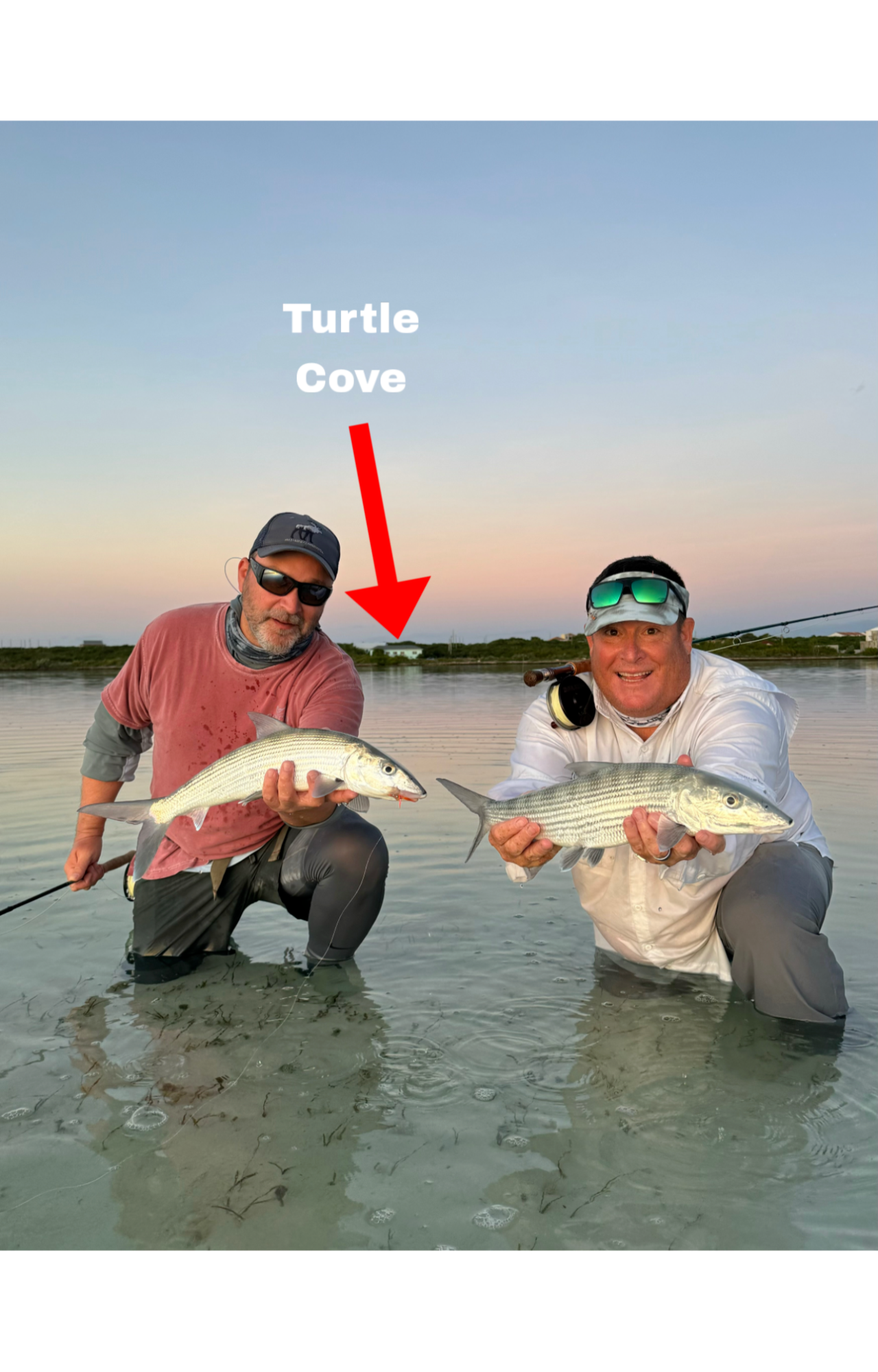 Two men in shallow water holding bonefish they caught while fishing at Turtle Cove during sunset.