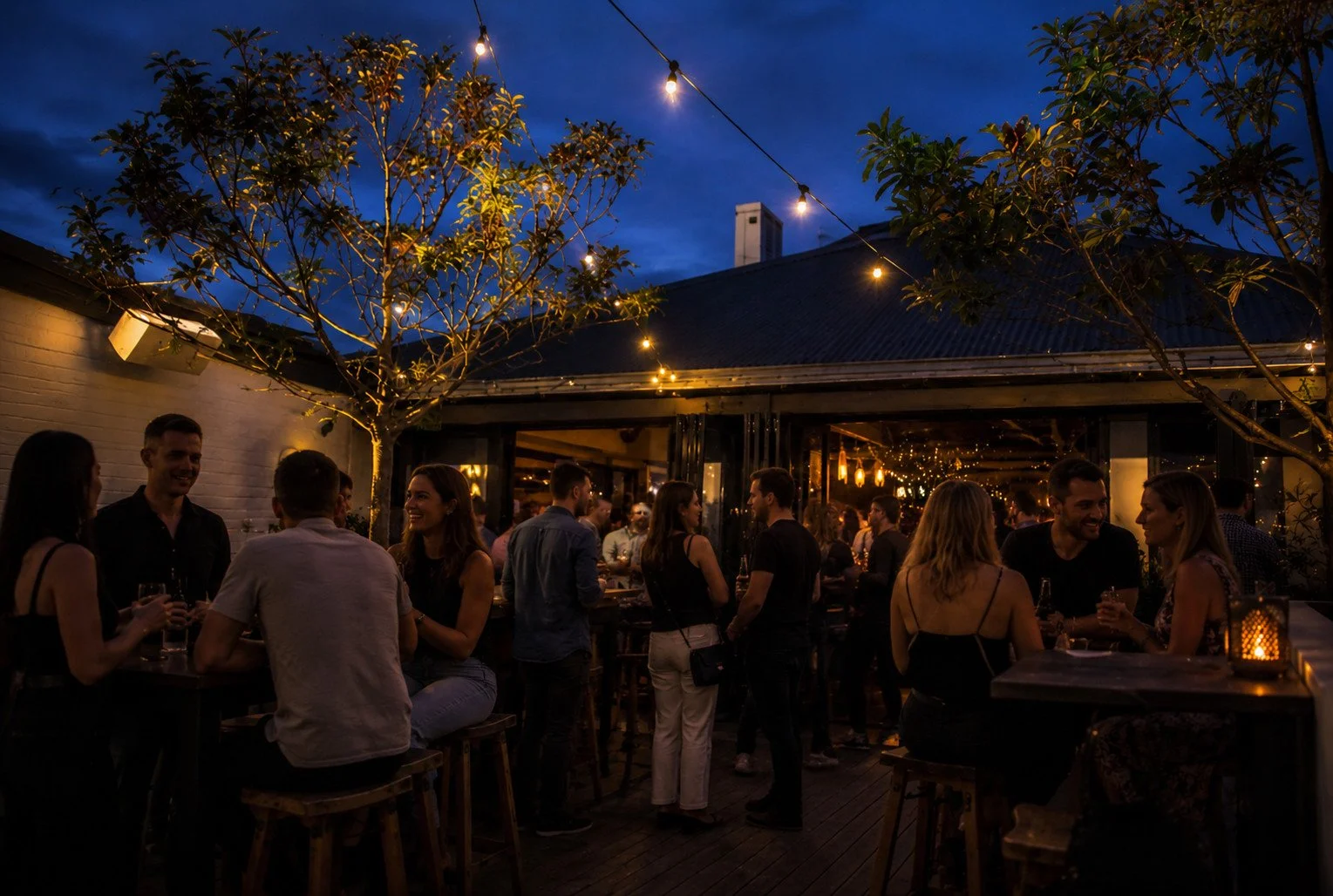 People socializing at an outdoor evening party with string lights and trees.