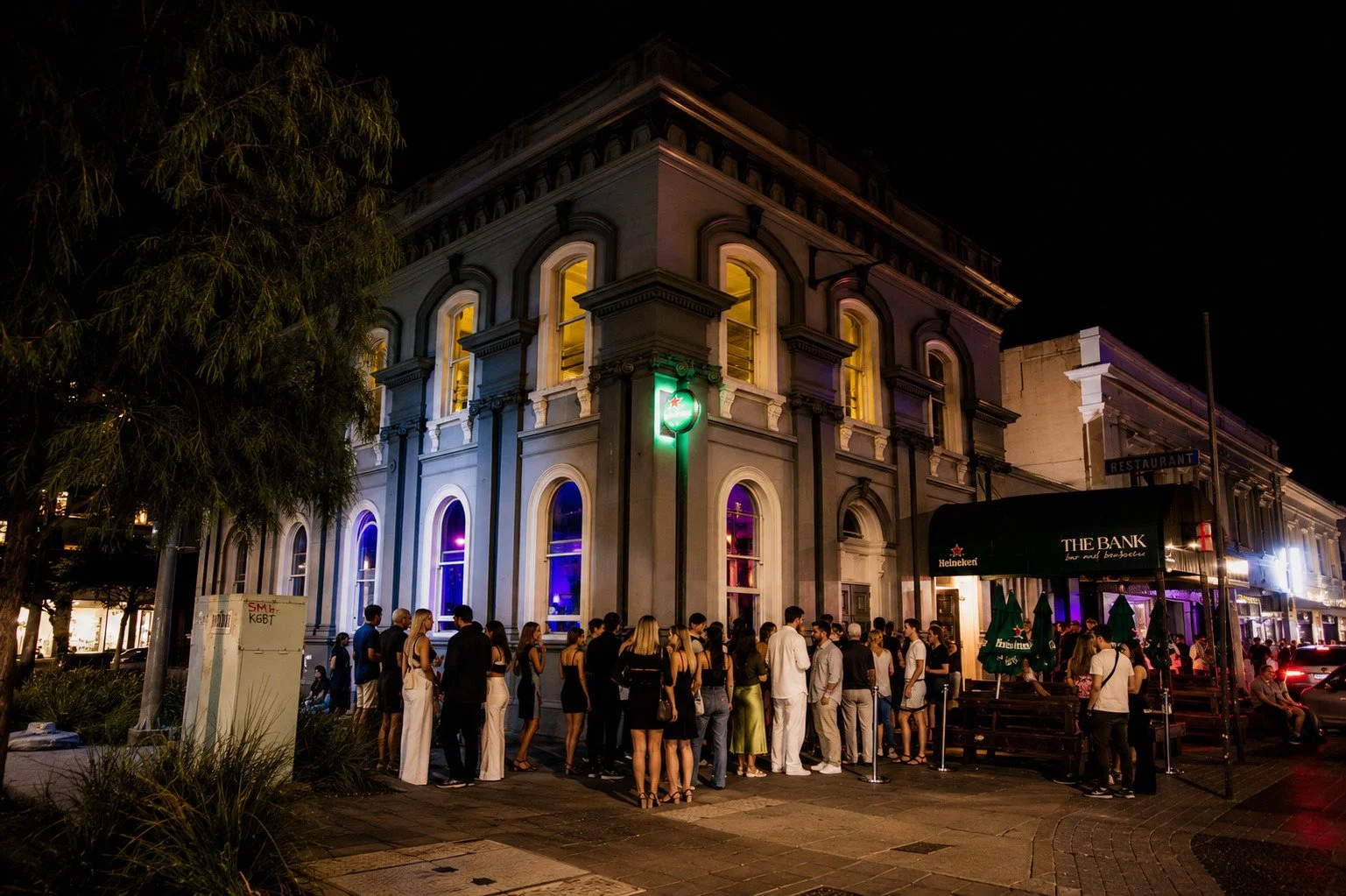 Night scene of a building with neon lights and a crowd of people waiting outside a bar or restaurant.