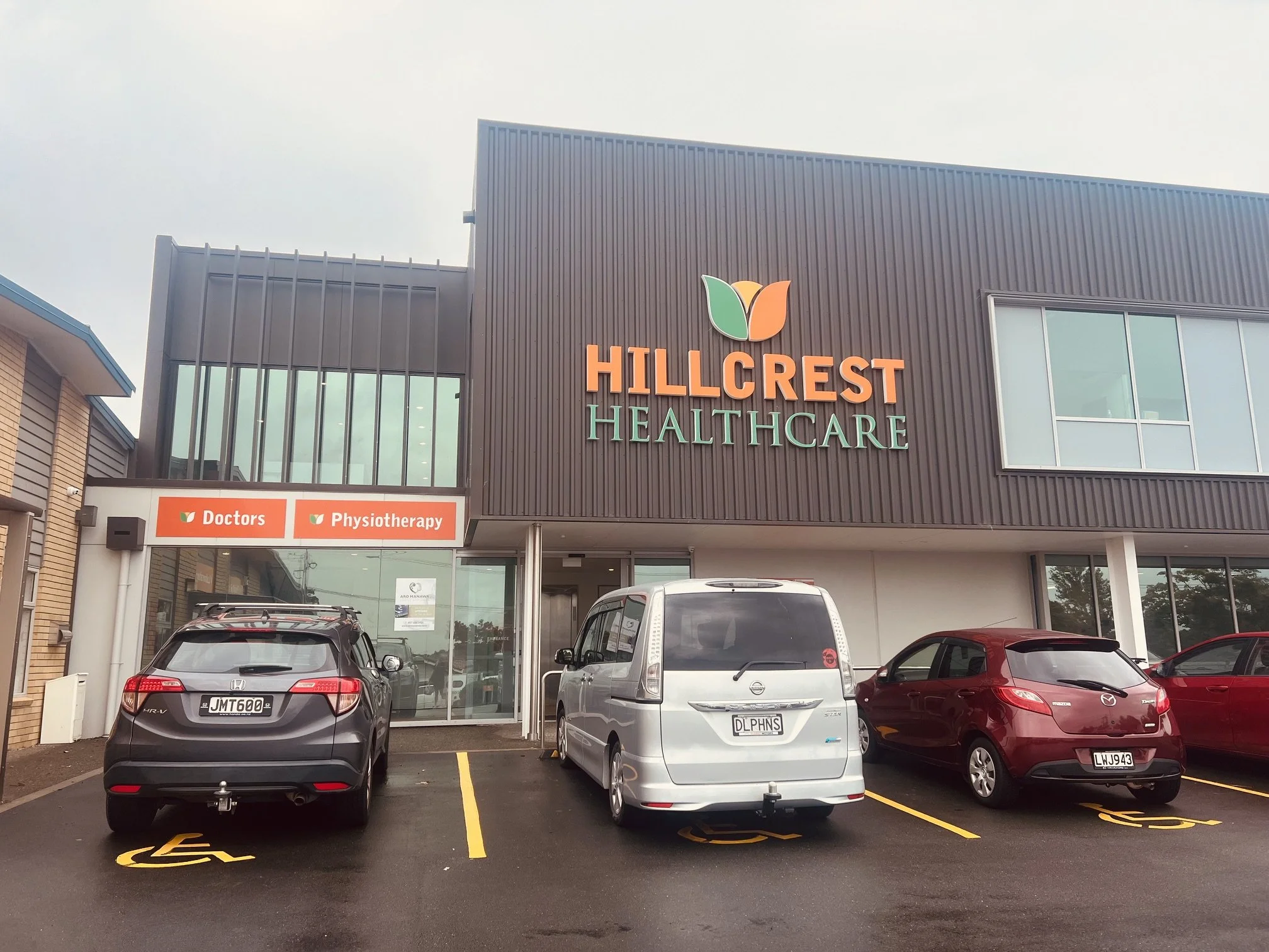 Parking lot in front of Hillcrest Healthcare with three cars parked, including accessible spaces, outside a modern medical building with signage for doctors and physiotherapy.