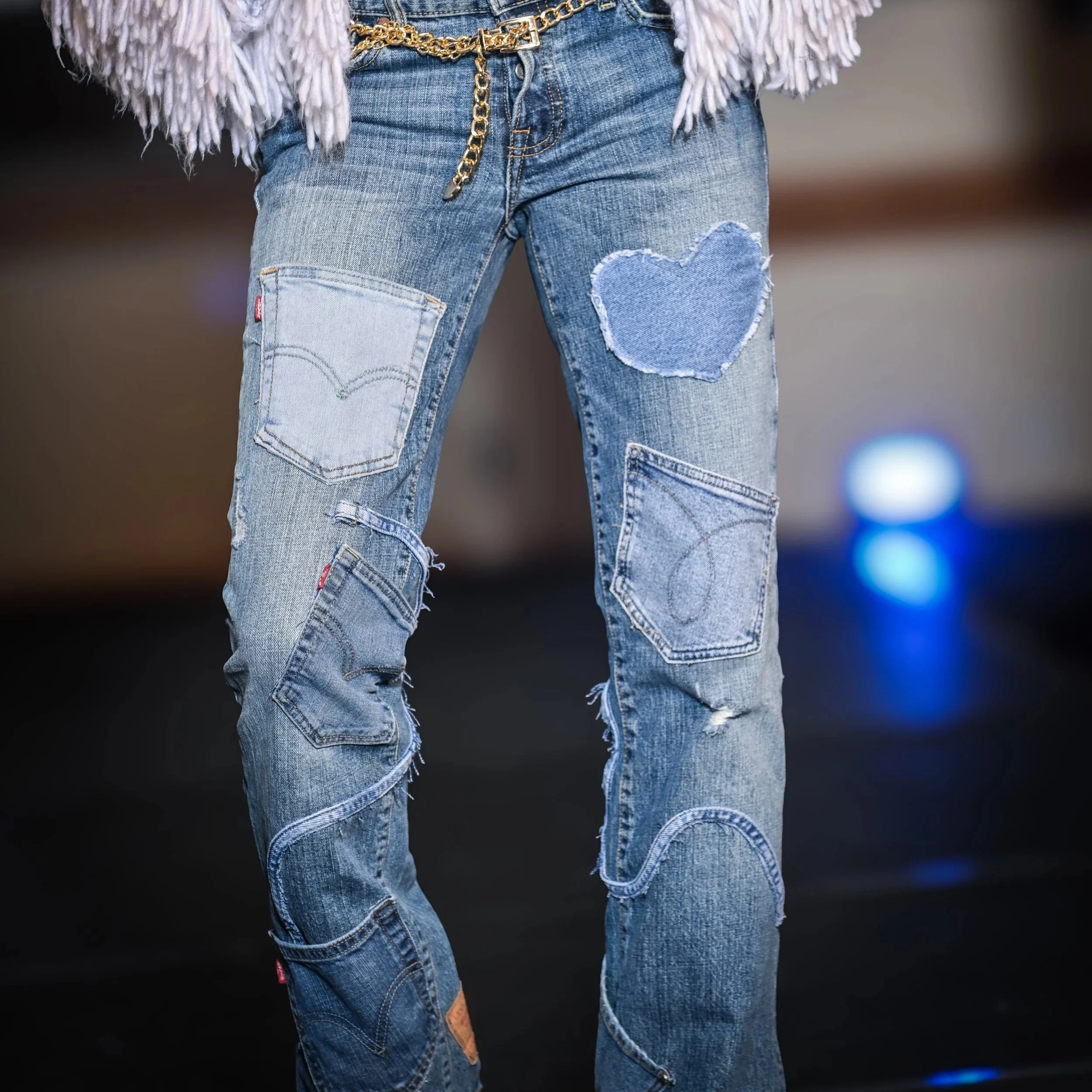 Close-up of distressed blue jeans with heart-shaped patches and pockets, paired with a gold chain belt.