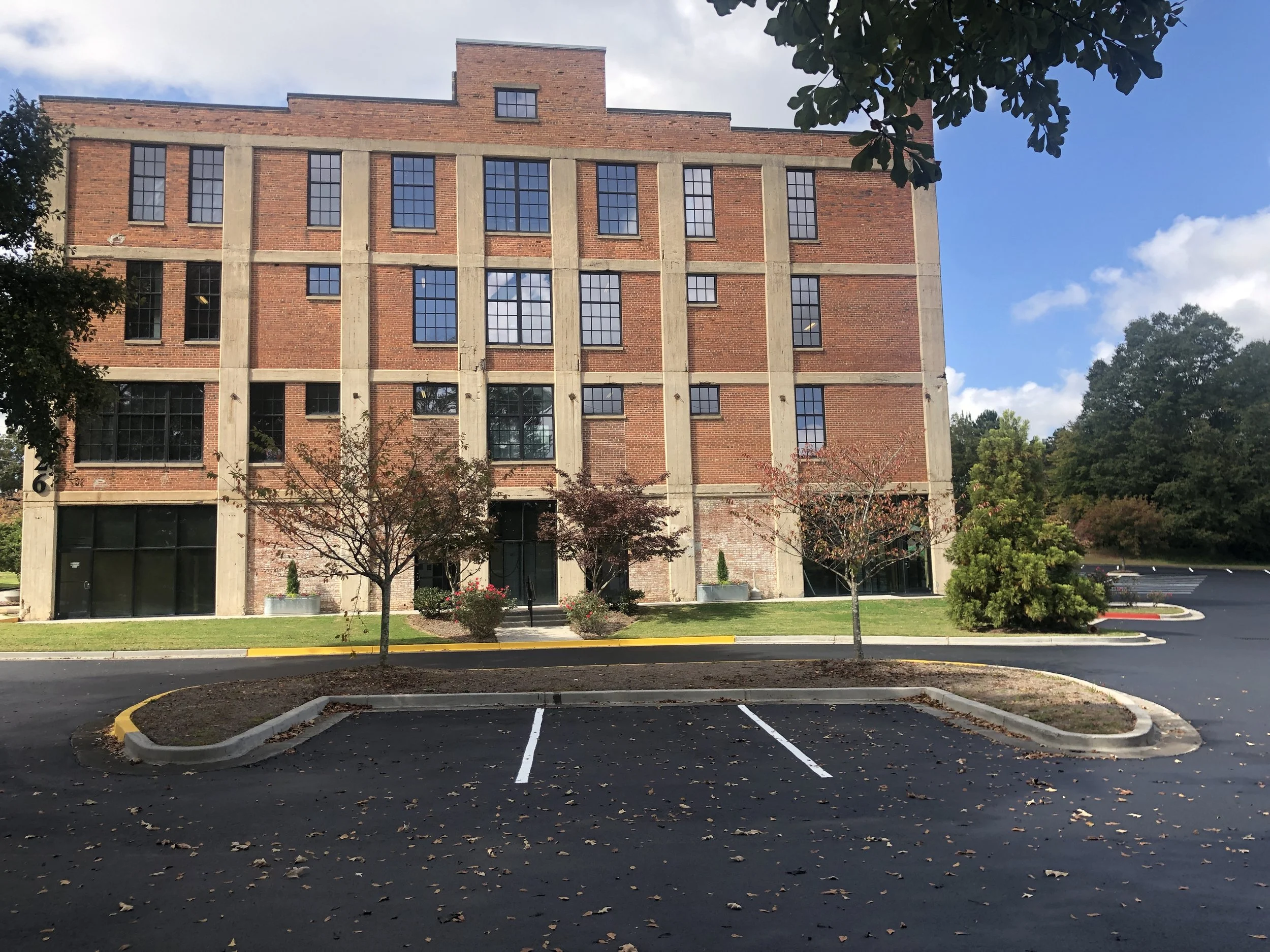 Empty parking lot in front of a brick building with large windows and small trees.