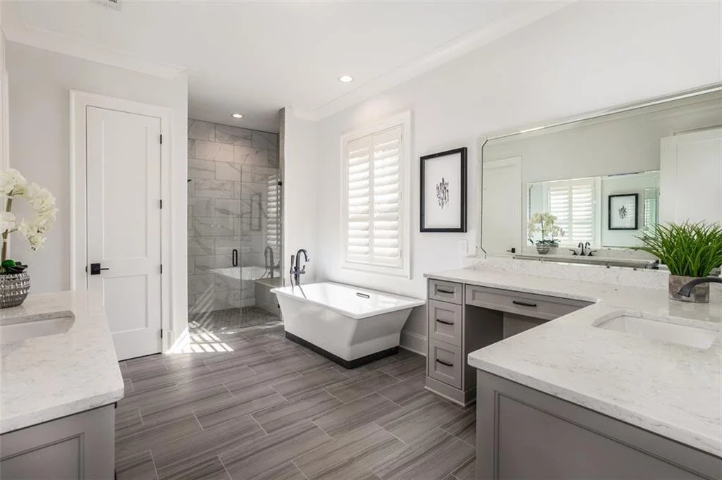 Modern bathroom with a bathtub, walk-in shower, gray cabinetry, large mirror, and window with shutters.
