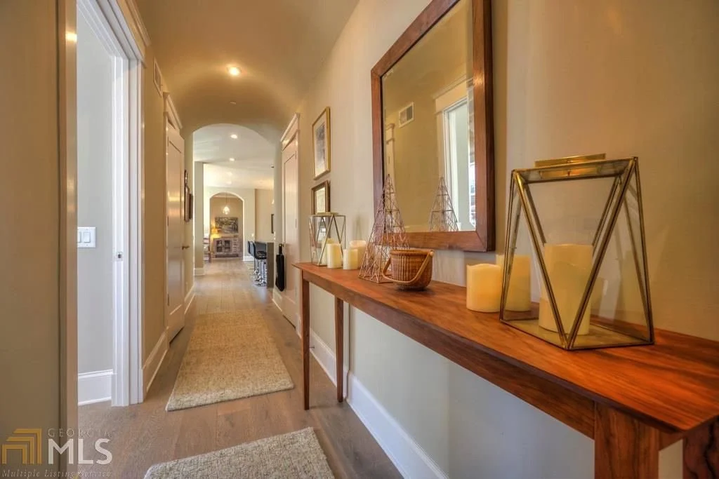Interior hallway with a wooden console table decorated with candles and decorative wire trees, a large mirror hanging above, and framed artwork on the walls.