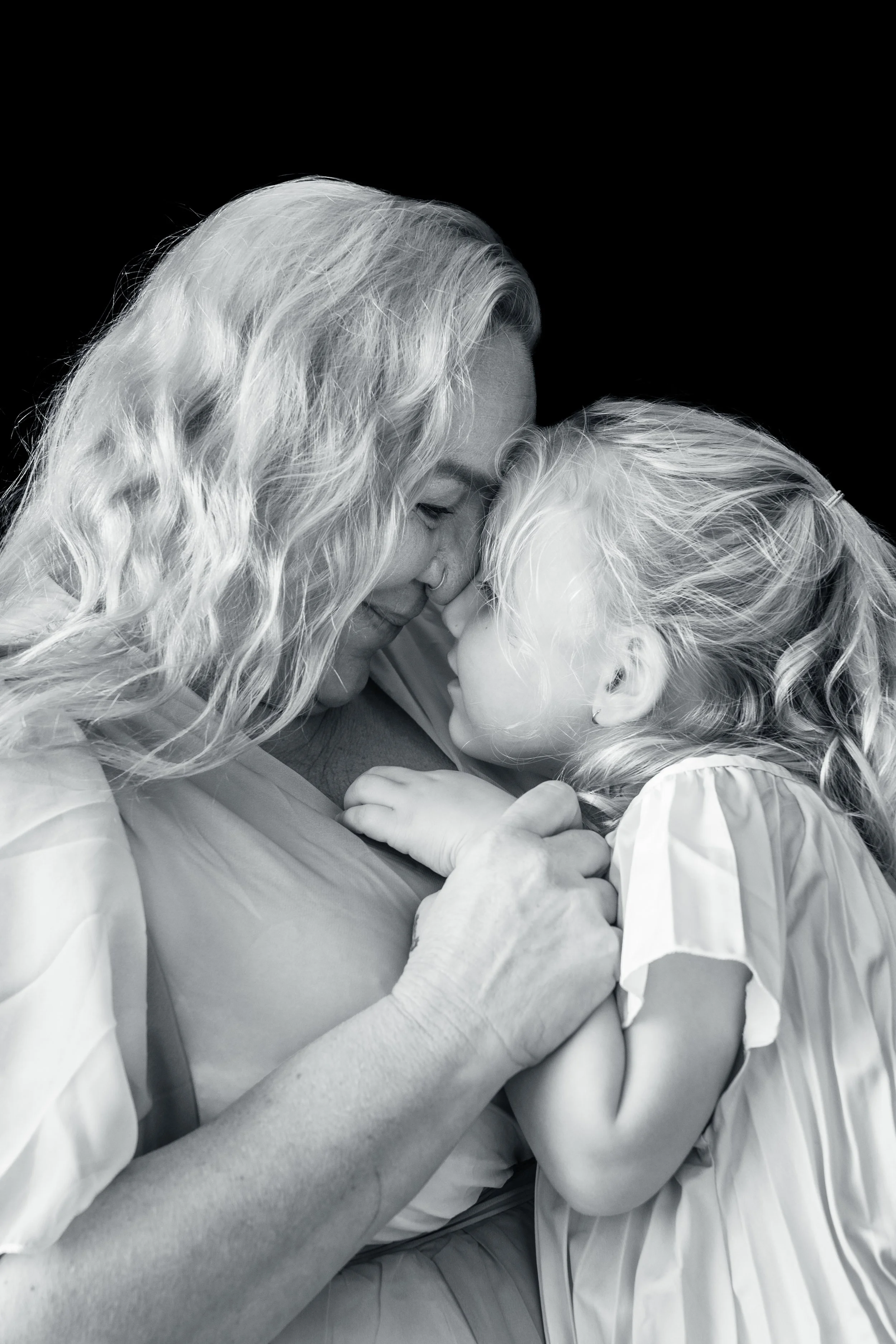 A black and white photo of an elderly woman and a young girl bonding closely, touching foreheads with eyes closed, conveying love and warmth.