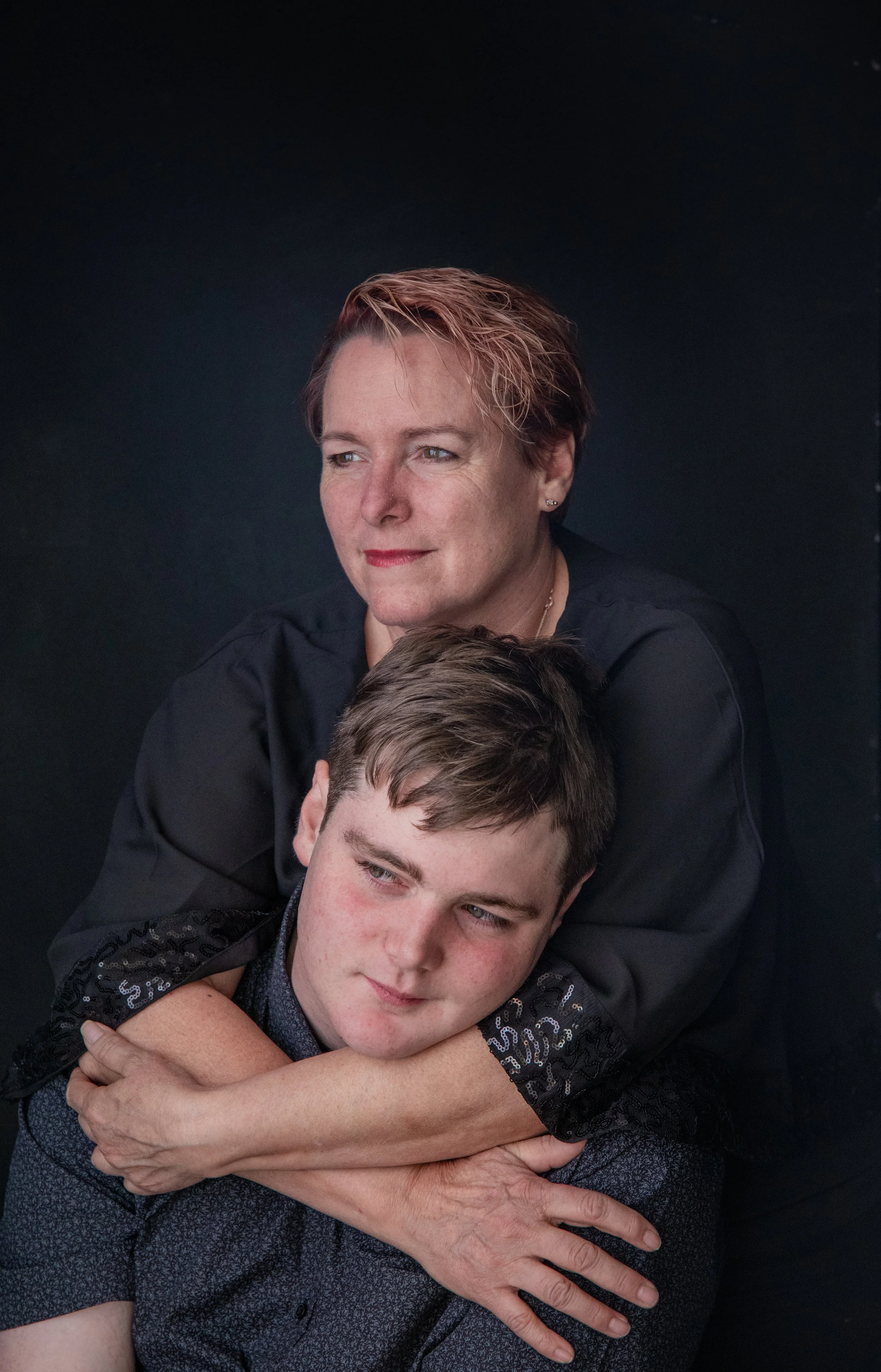 A woman embracing a young man against a black background.