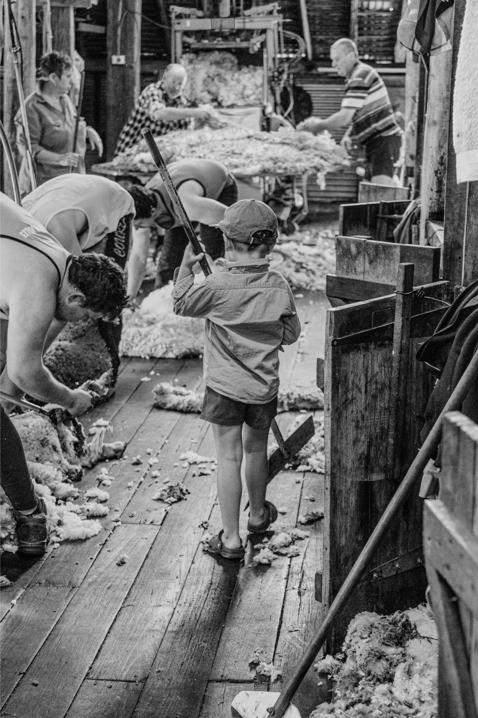 People working with sheep wool and a young boy holding a tool in a workshop.