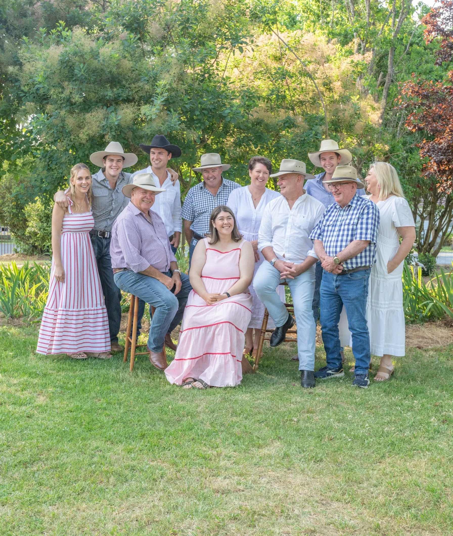 A group of people outdoors in a garden, wearing casual clothing and cowboy hats, smiling and posing for a photo.
