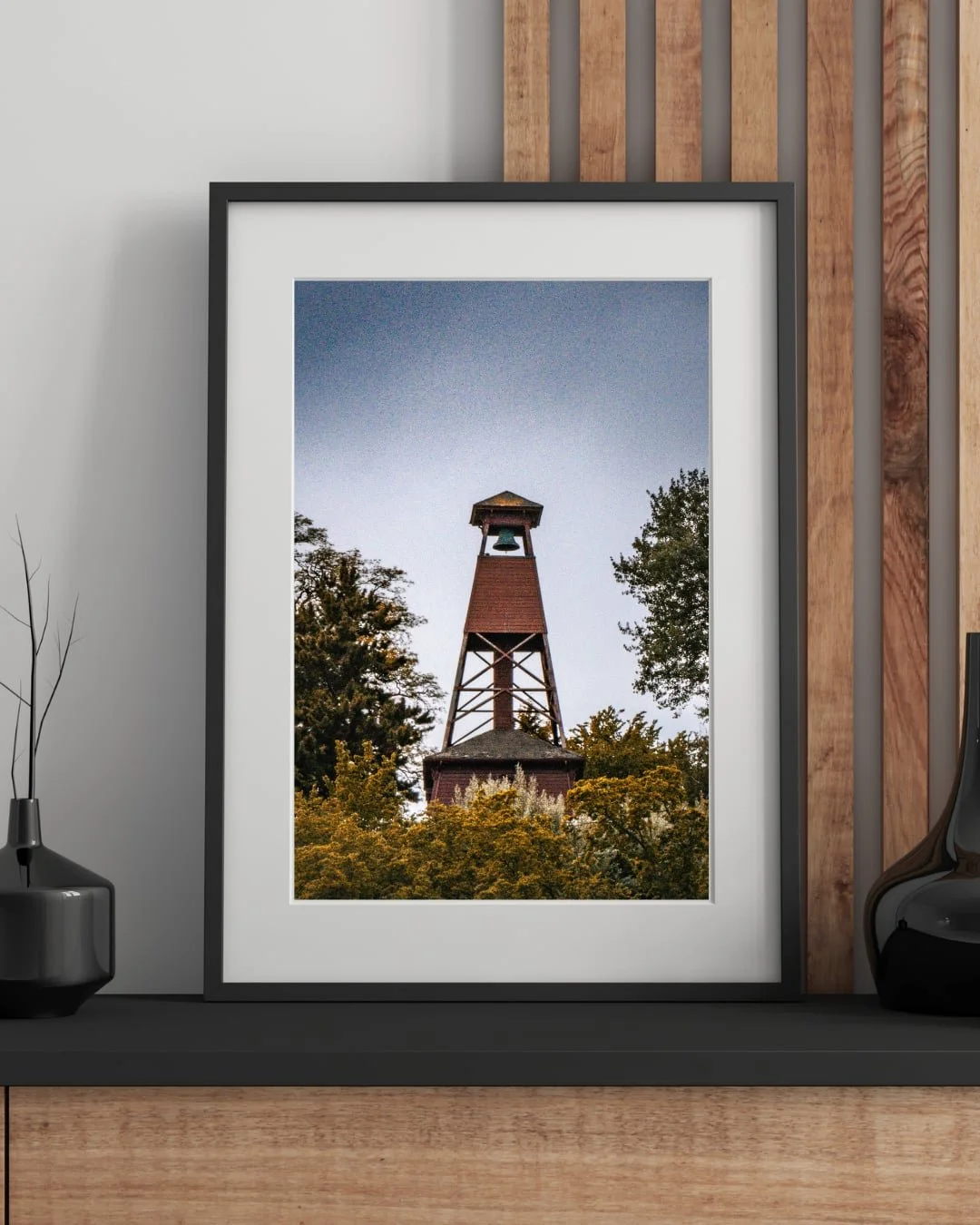 A historic red wooden fire tower sits atop a coastal hill with autumn foliage and a gritty texture overlay. The sky is blue and clear in the background