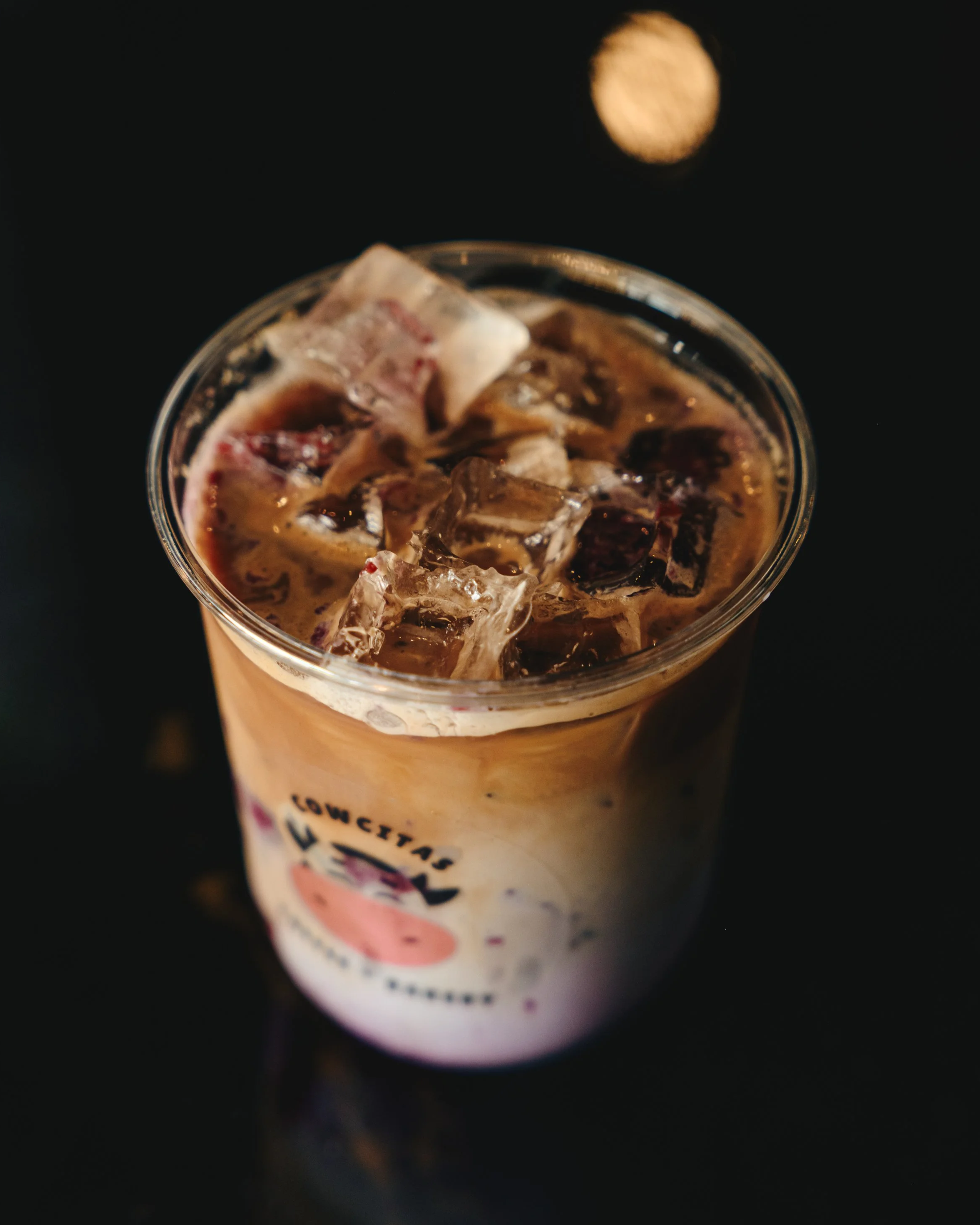 A close-up photo of a beverage in a glass filled with ice cubes, with a dark background and a moon visible in the sky.