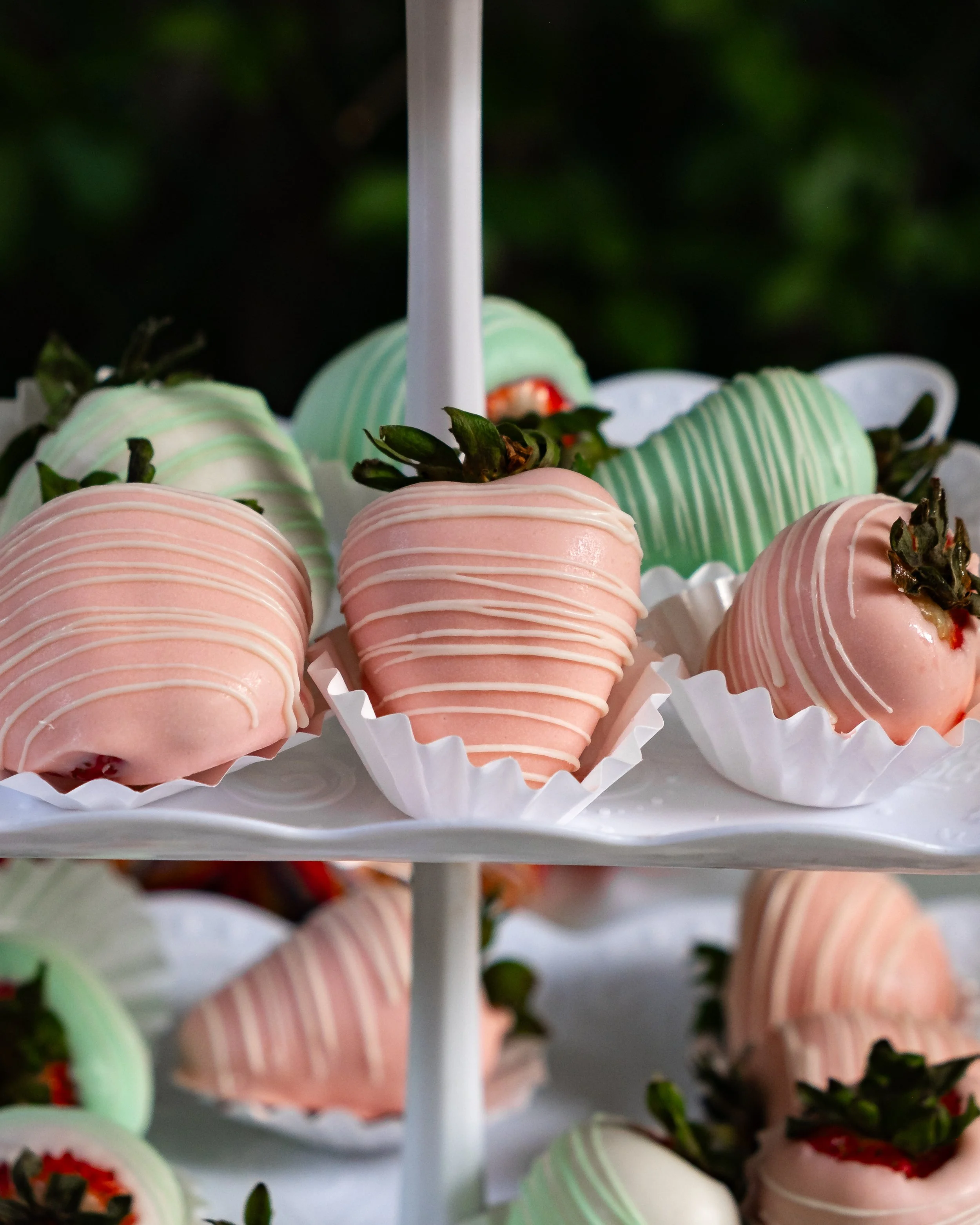 Close-up of pink and green chocolate-covered strawberries on a white tiered tray.