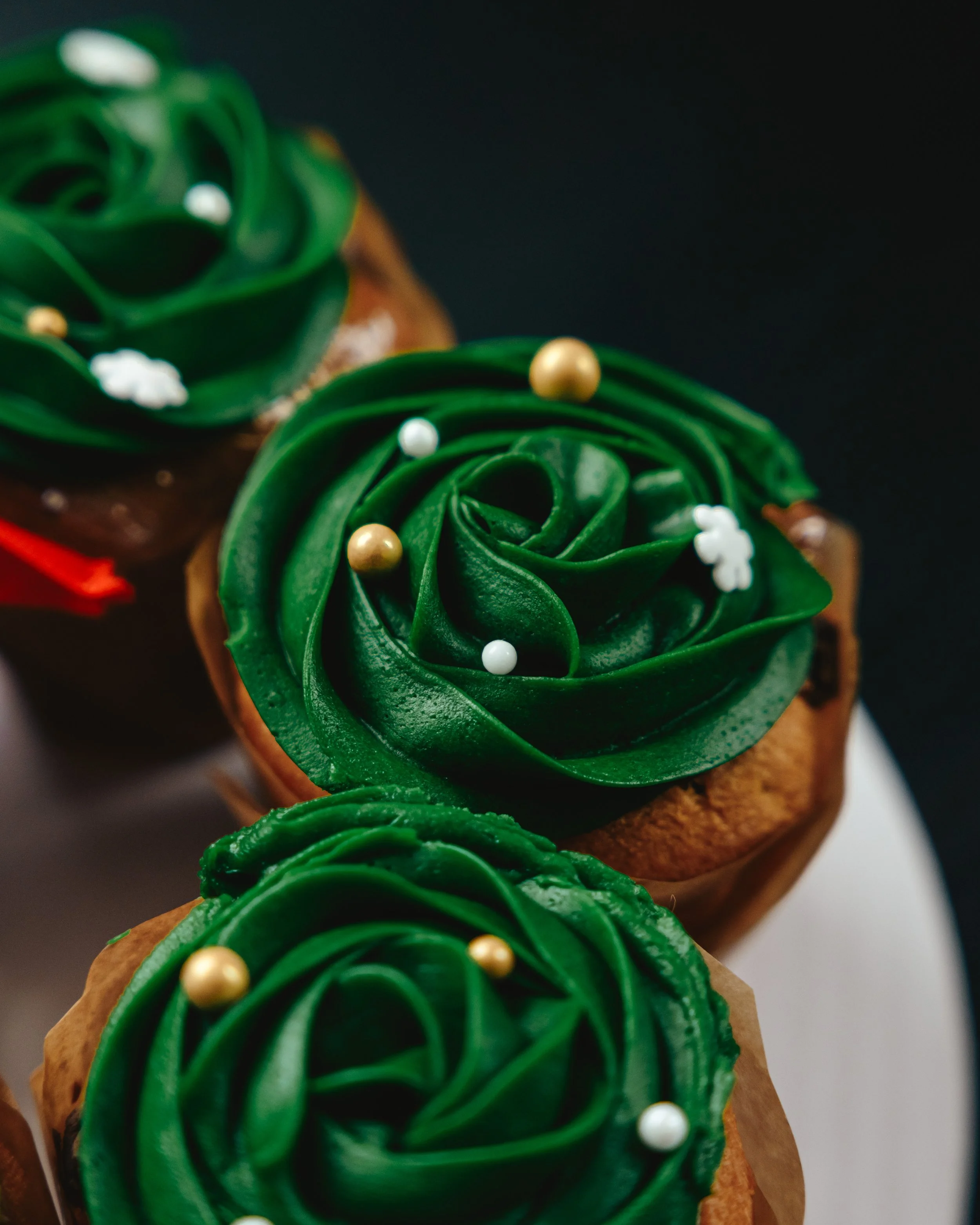 Close-up of cupcakes decorated with green rose-shaped frosting and small edible pearls.