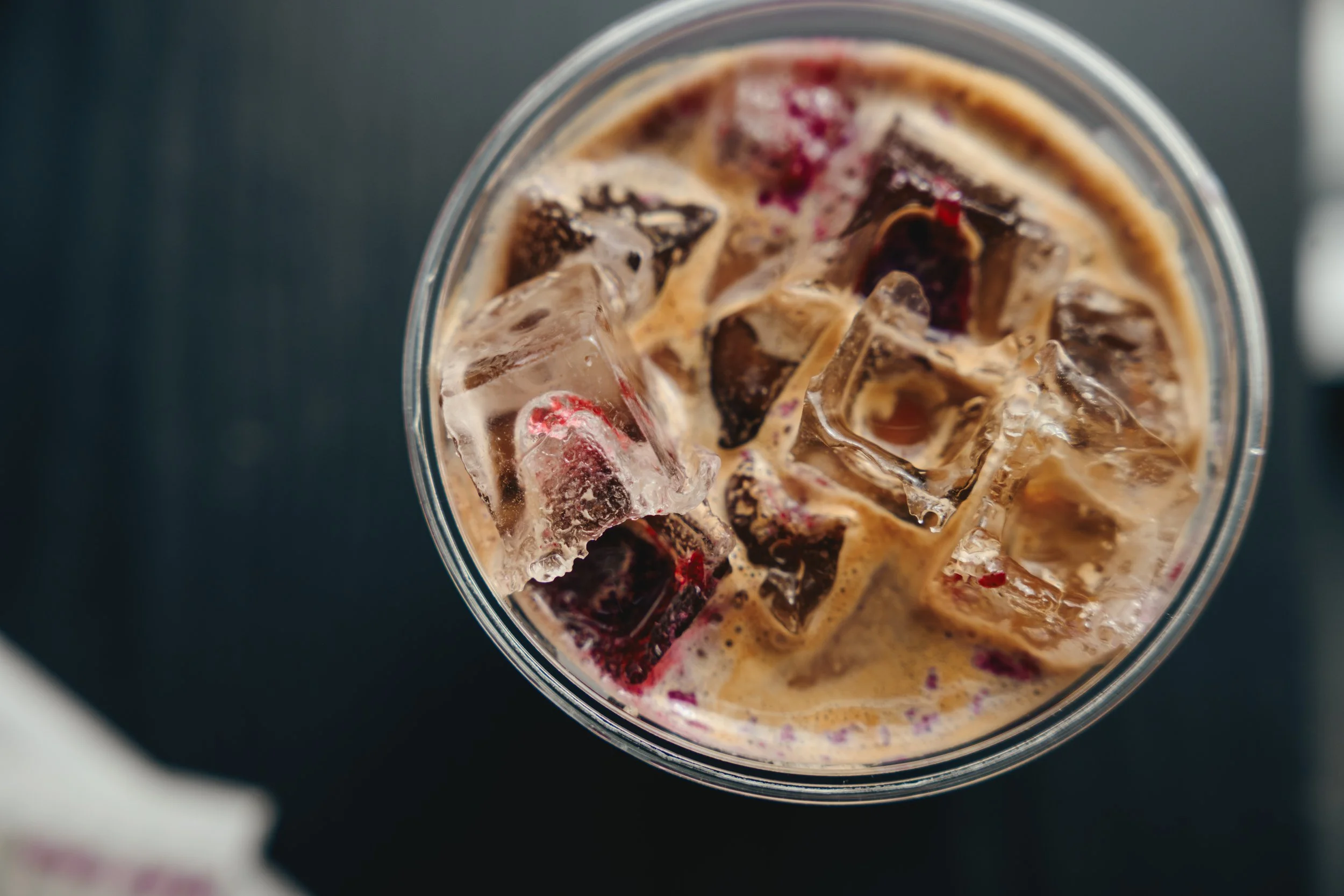 Top-down view of a glass filled with ice cubes and dark-colored iced coffee.