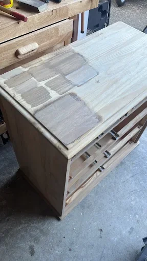 A woodworking project showing a wooden cabinet or side table in the process of being assembled, with a partially sanded top surface.