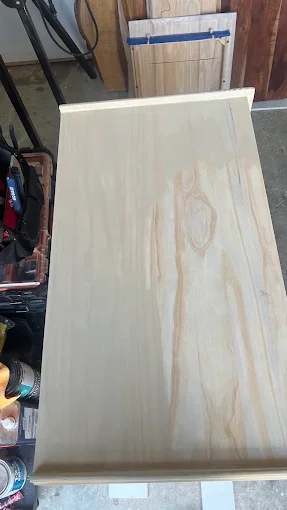 A large, unfinished wooden board on a workbench in a workshop.