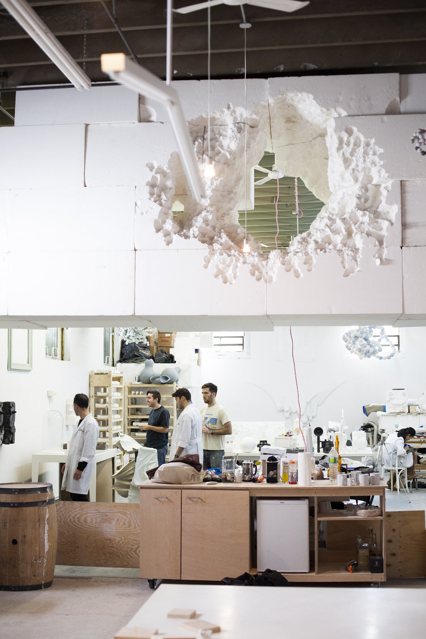 Interior of a ceramics or art studio with a group of people working and a large, irregularly shaped hole in a white wall or ceiling feature.