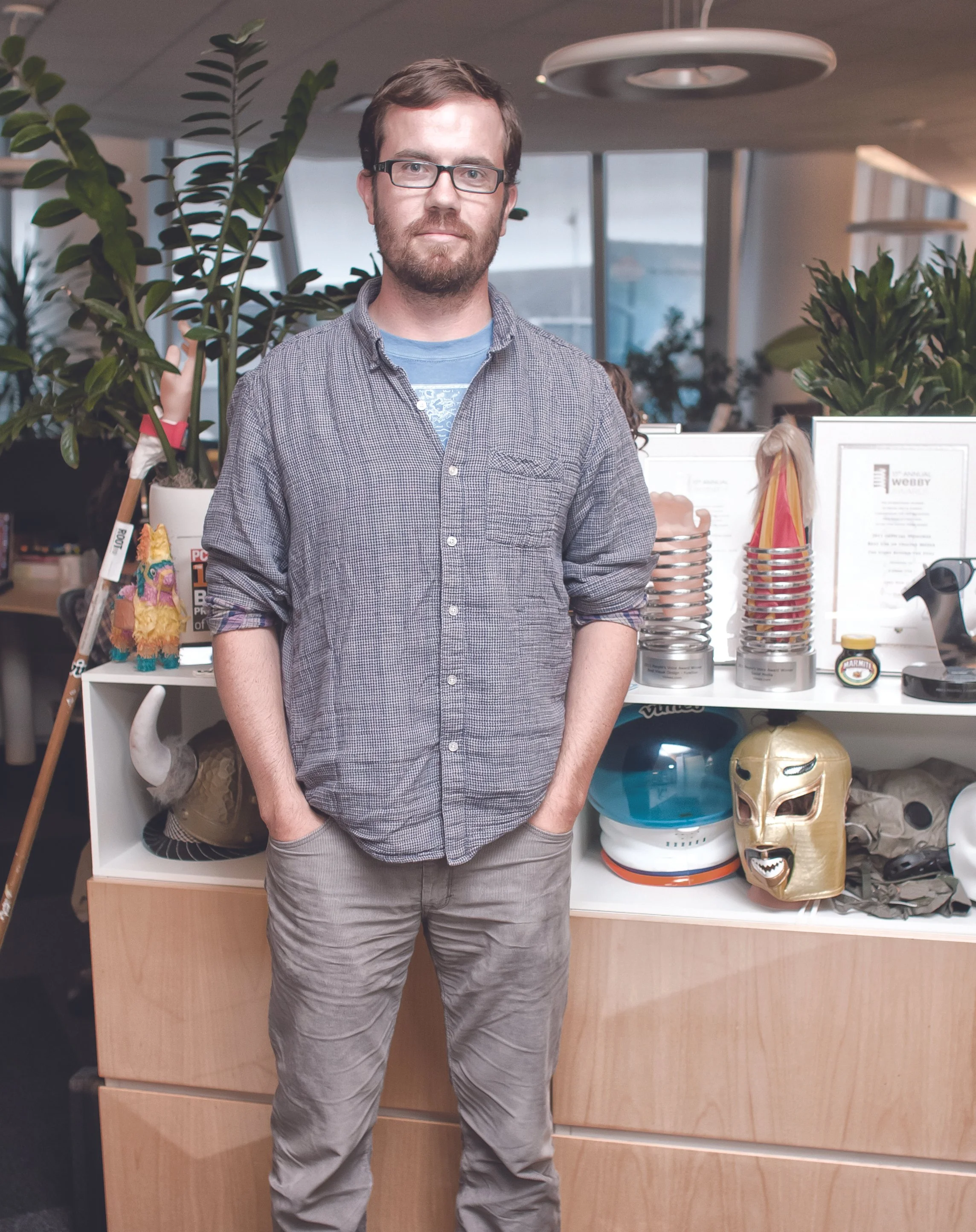A man with glasses standing in front of a desk with plants, masks, awards, and various objects at an office.