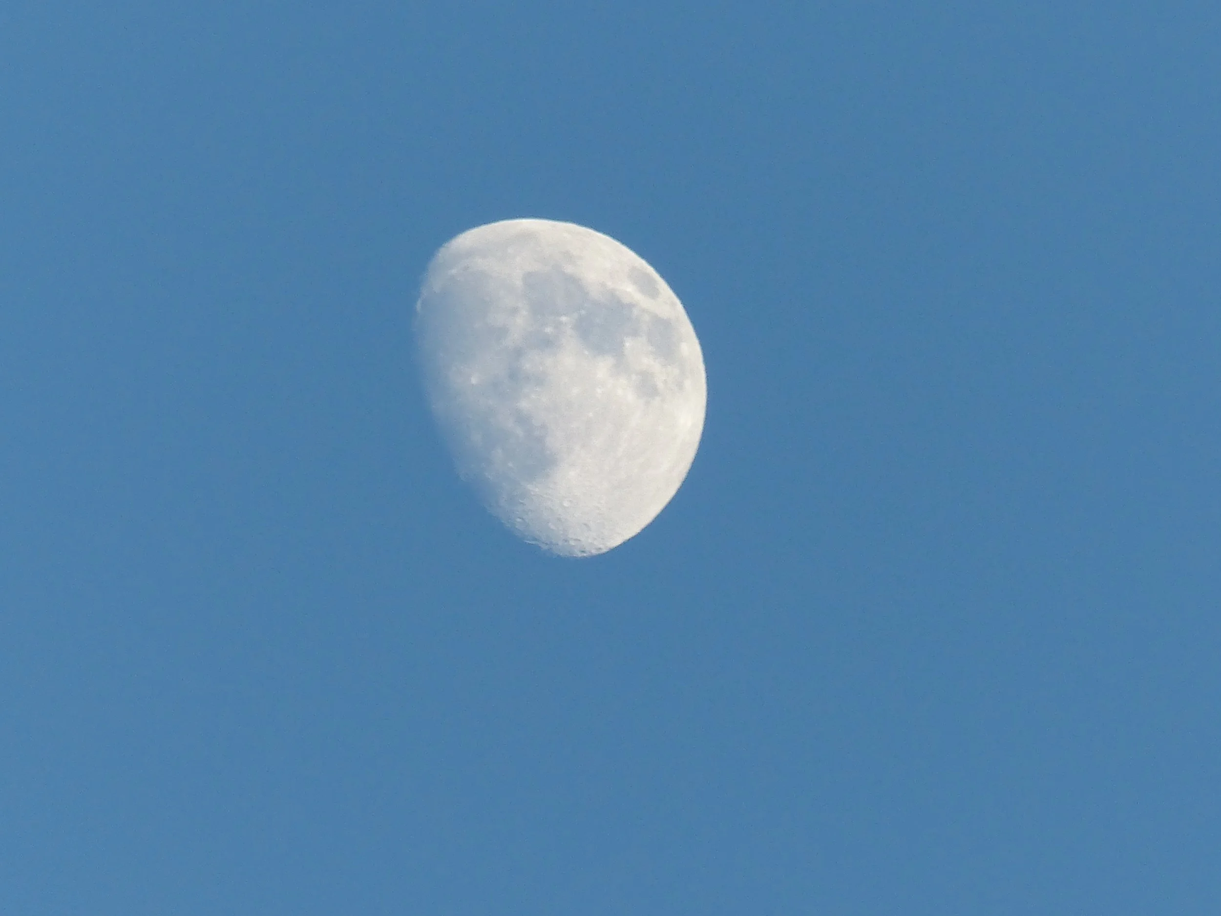 The image shows the moon in a crescent phase against a clear blue sky.