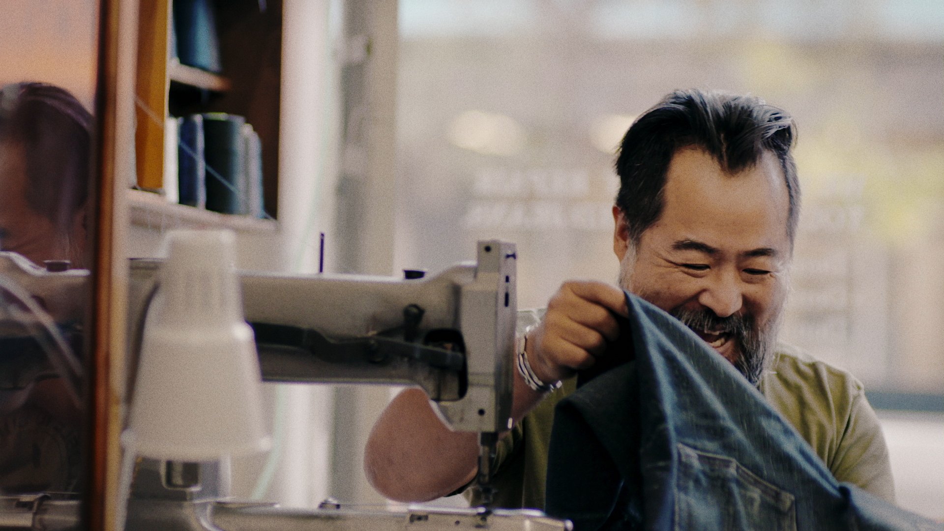 A man examining a pair of jeans in a clothing store with a sewing machine in the foreground