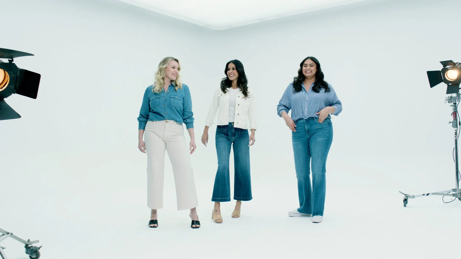 Three women standing in a photography studio with bright lighting, smiling and looking at each other.