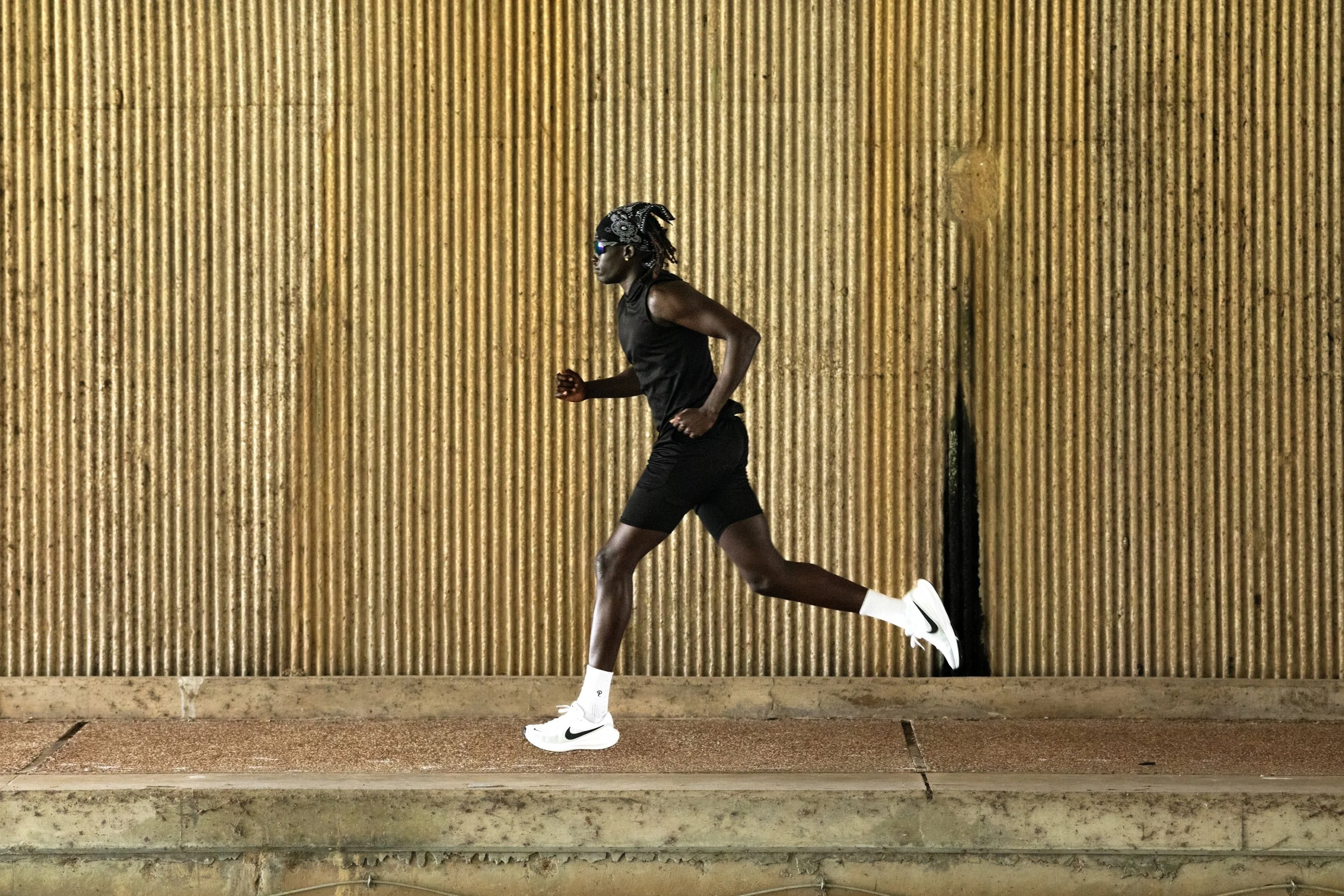 A person in athletic gear running on a track with a striped, yellowish wall in the background.
