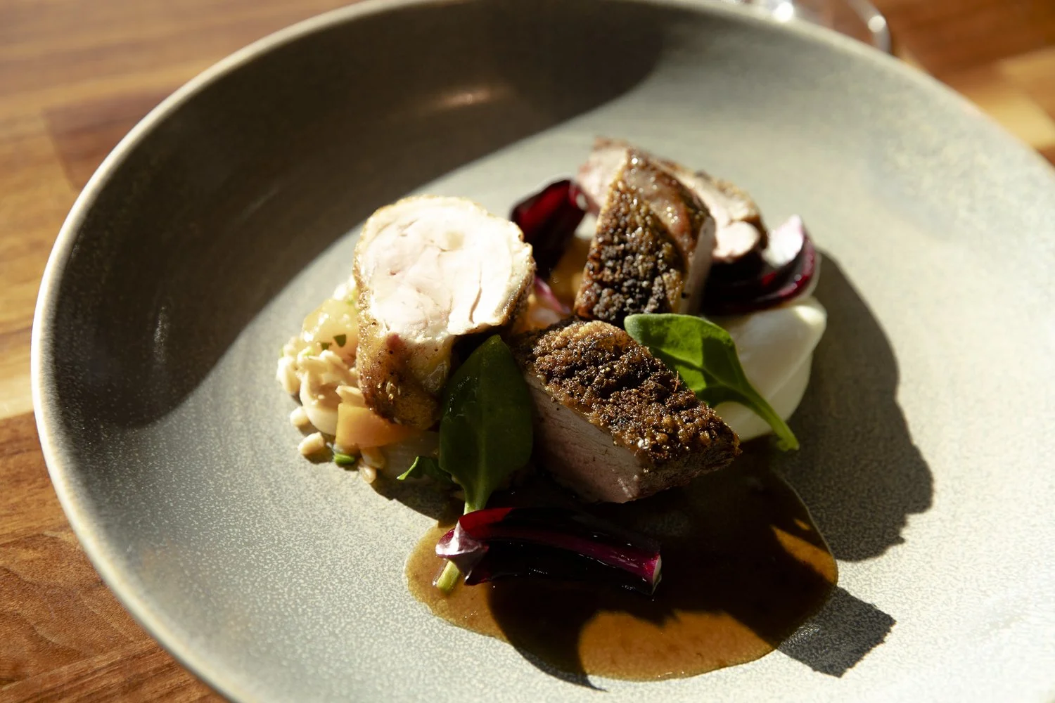Three slices of cooked chicken with a crispy herb crust, served on a bed of mashed potatoes, garnished with leafy greens and red onion, with drizzle of dark gravy on a green ceramic plate.