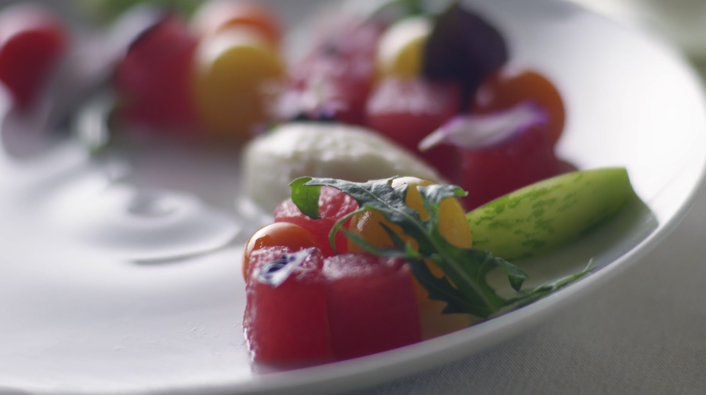 Close-up of a salad with watermelon, cherry tomatoes, cucumber, and greens on a white plate.