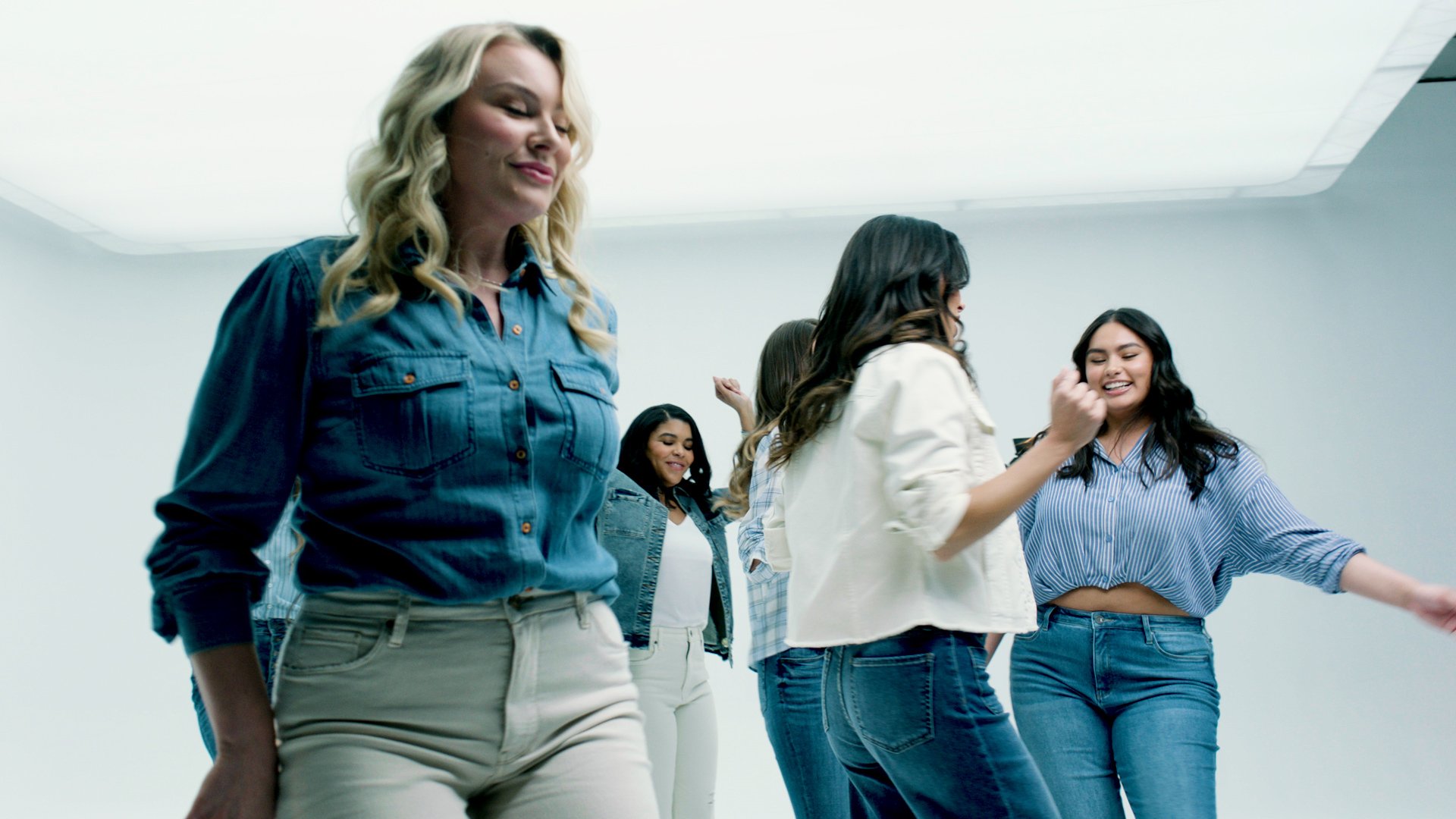 Group of young women dancing and smiling in a bright white room.