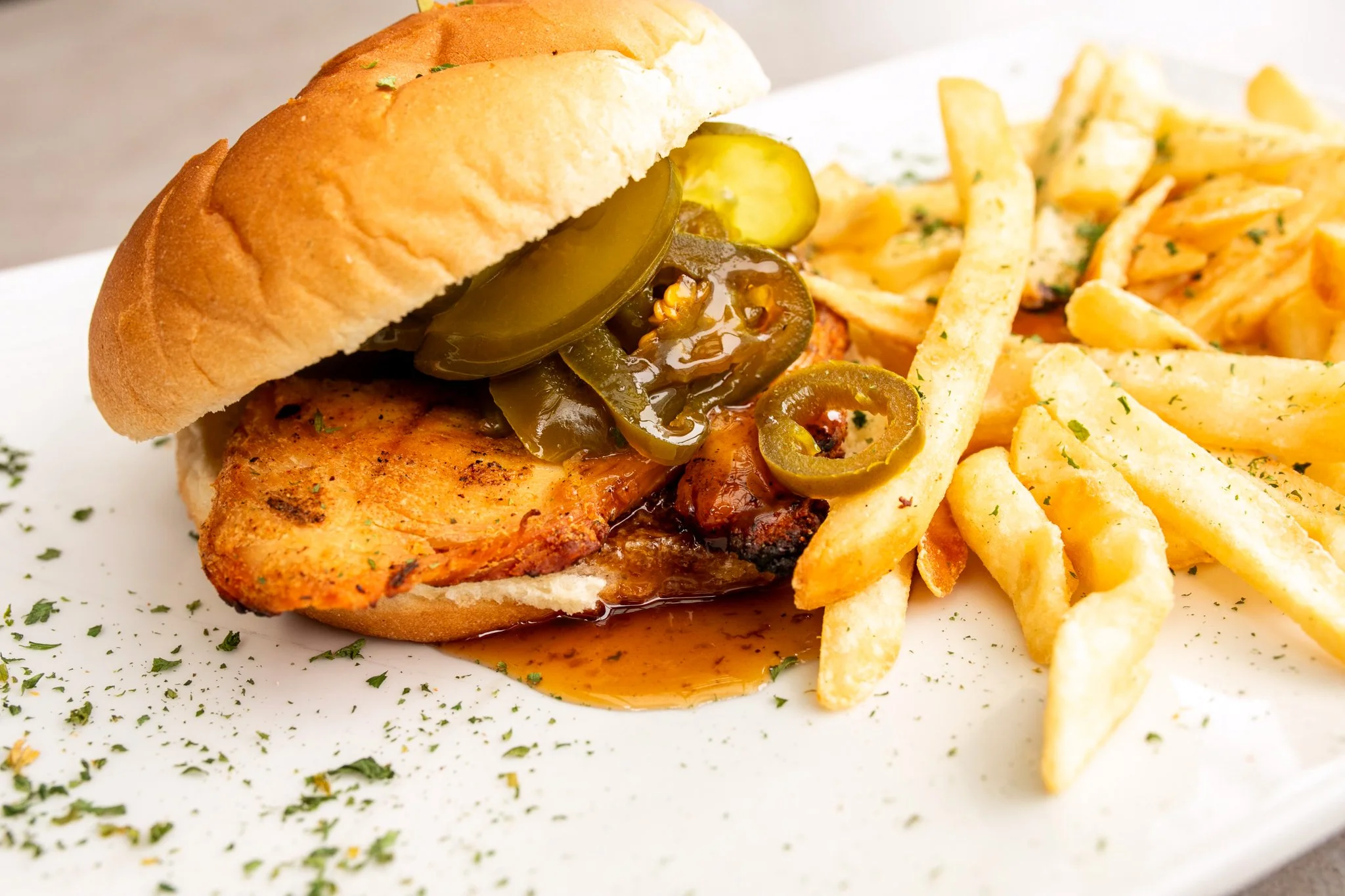Fried chicken sandwich with pickles and fries on a white plate