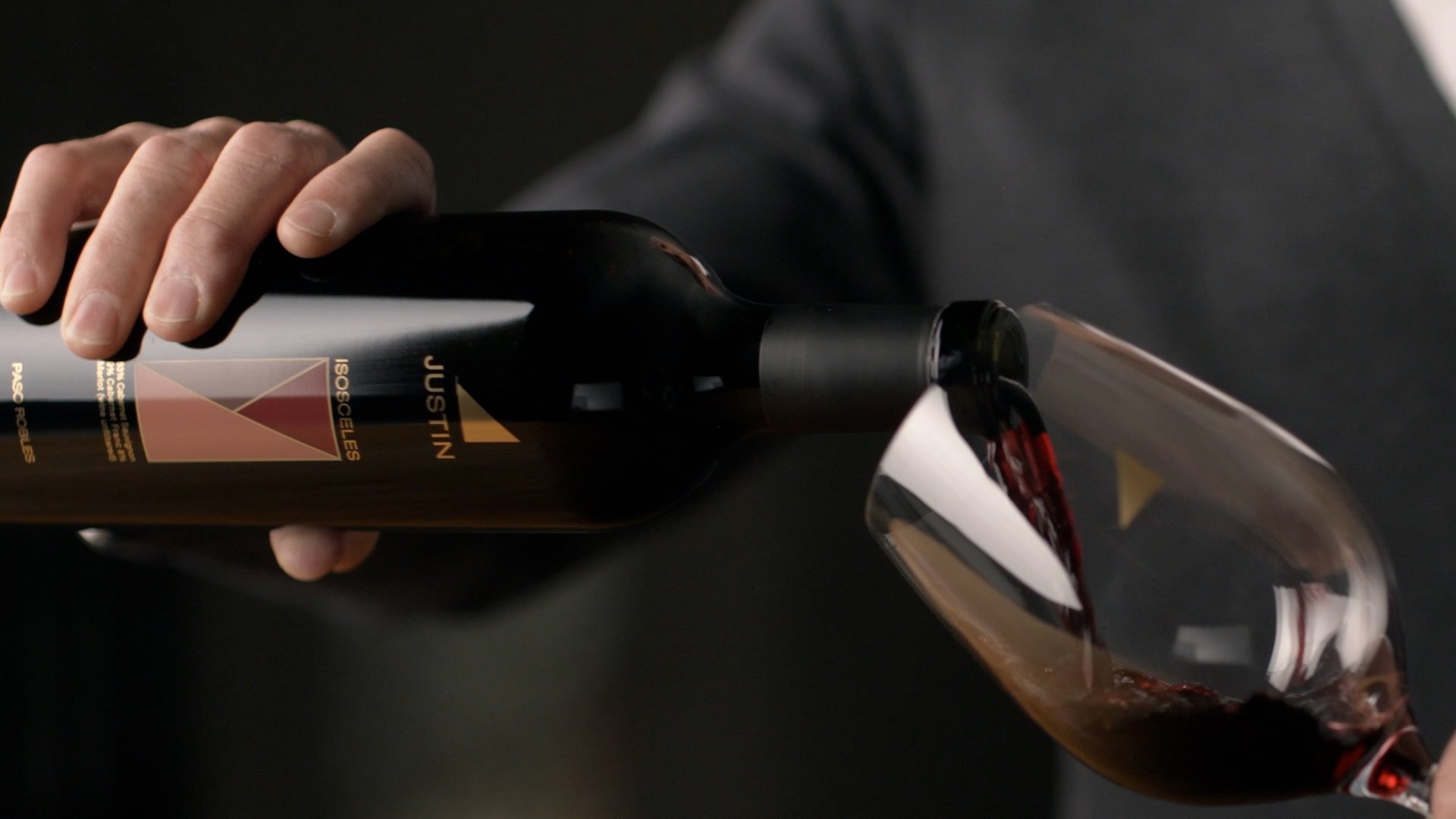 A person in a black long-sleeve shirt pours red wine from a bottle into a wine glass.