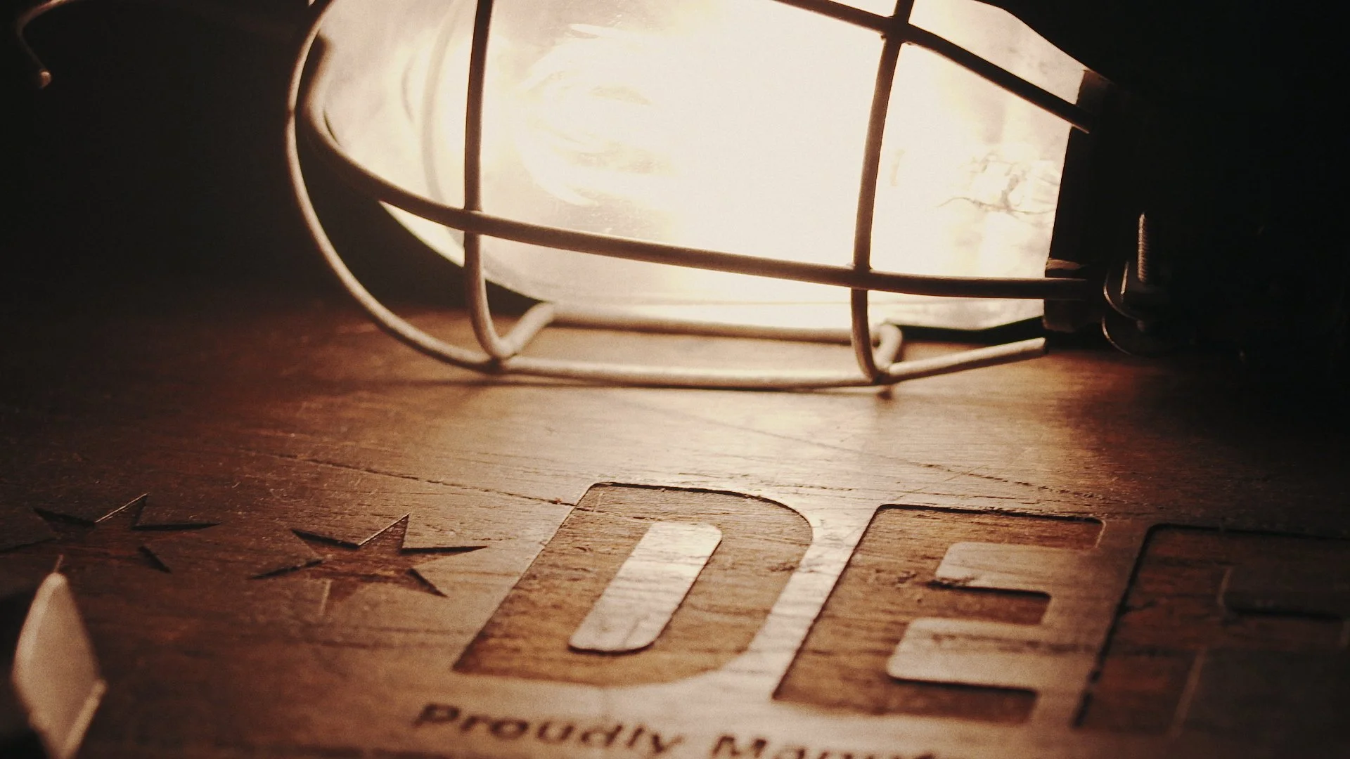 A close-up of a vintage industrial-style light illuminating a wooden surface with cut-out letters spelling 'IDEA' and star shapes, creating a warm and cozy glow.