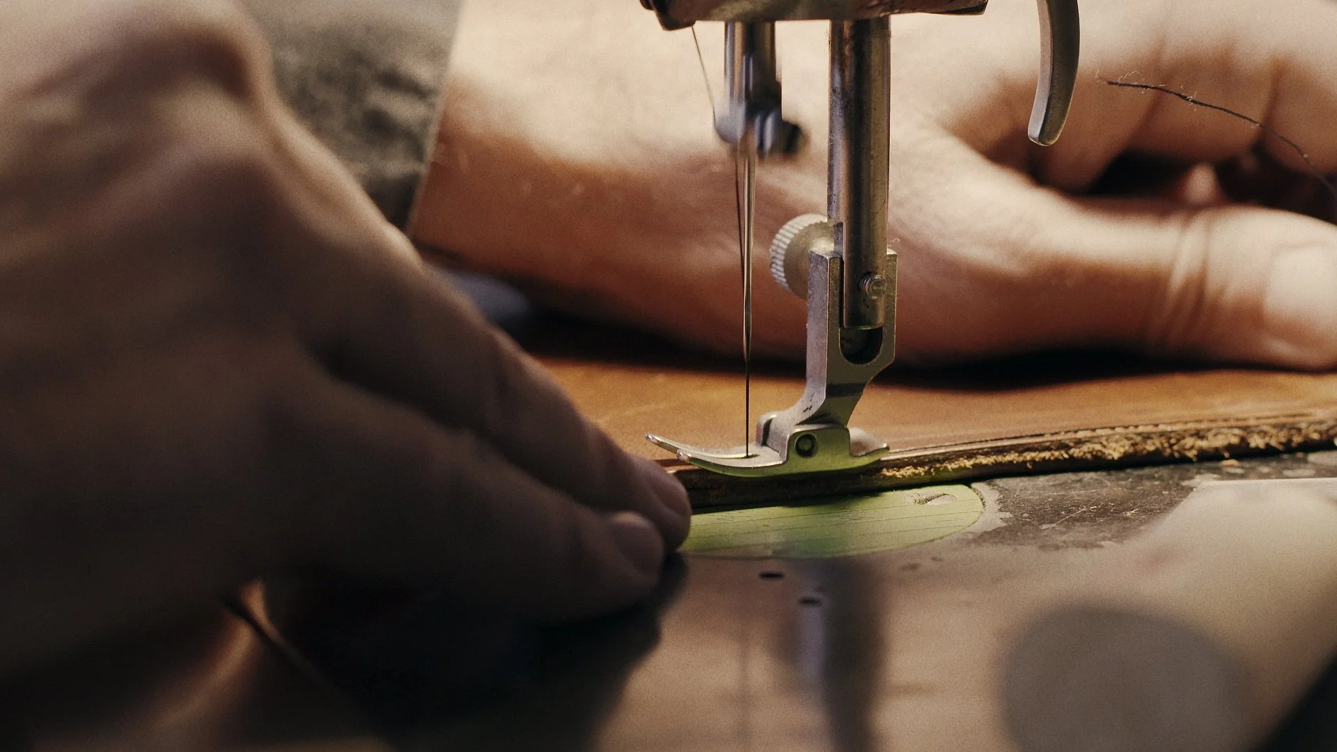 Close-up of a person sewing leather using a sewing machine.