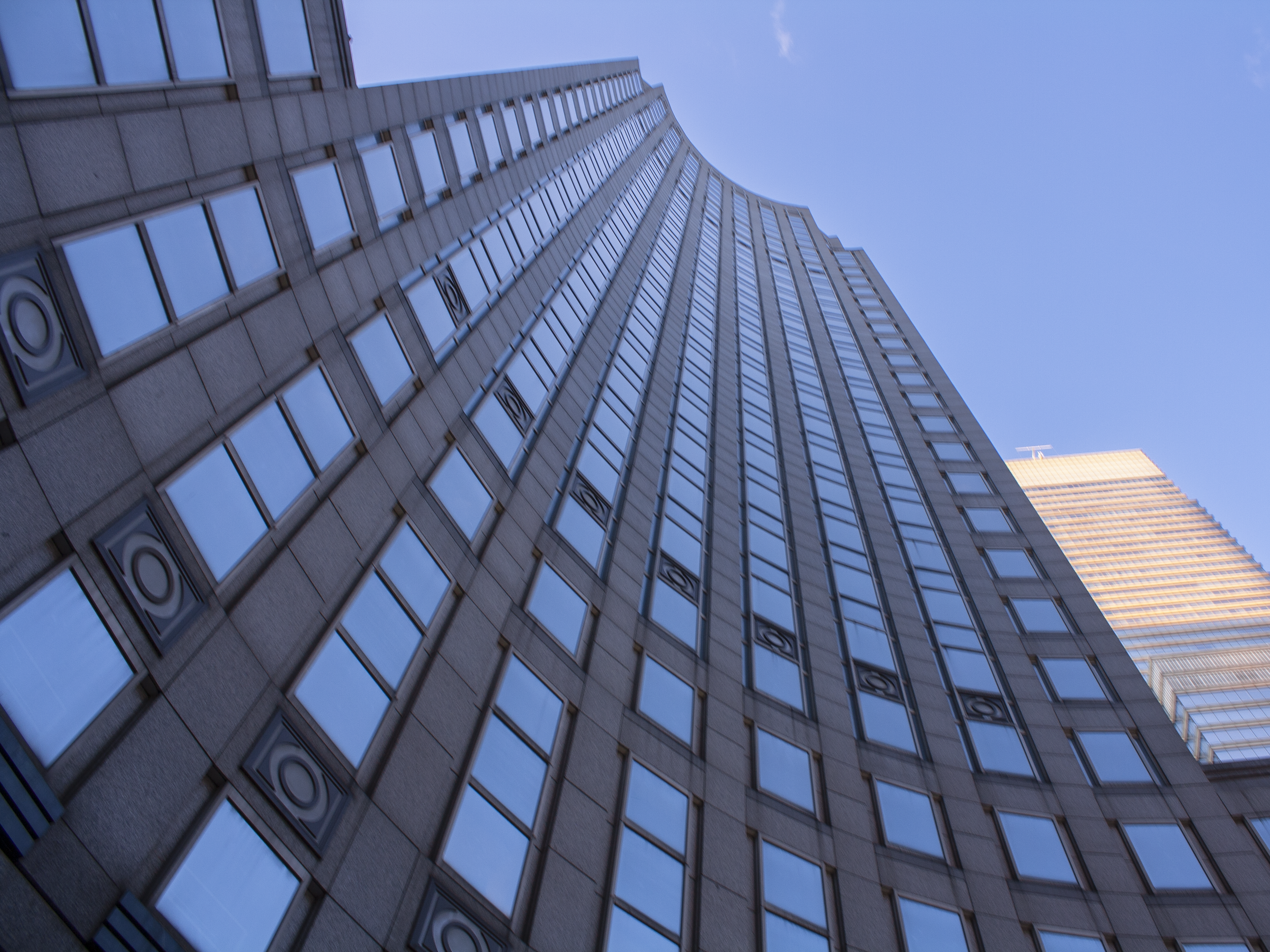 A tall modern skyscraper with reflective glass windows and decorative circular patterns on its facade, taken from the ground looking upward toward blue sky.