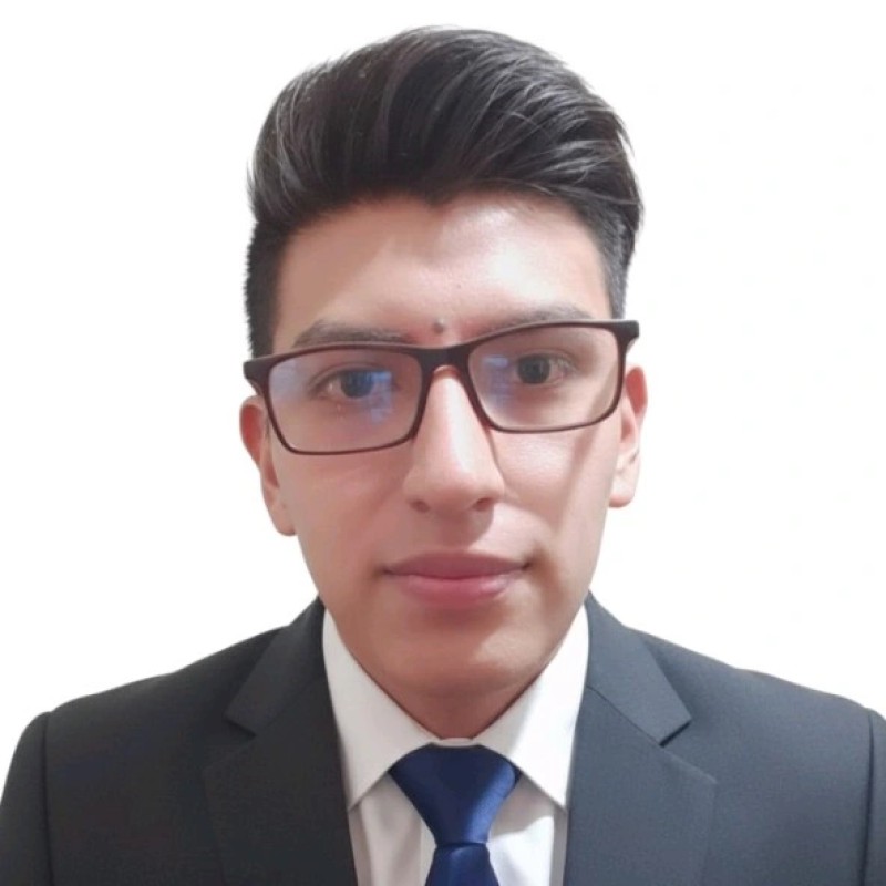 A young man wearing glasses, a white shirt, a dark suit, and a blue tie, looking directly at the camera with a neutral background.