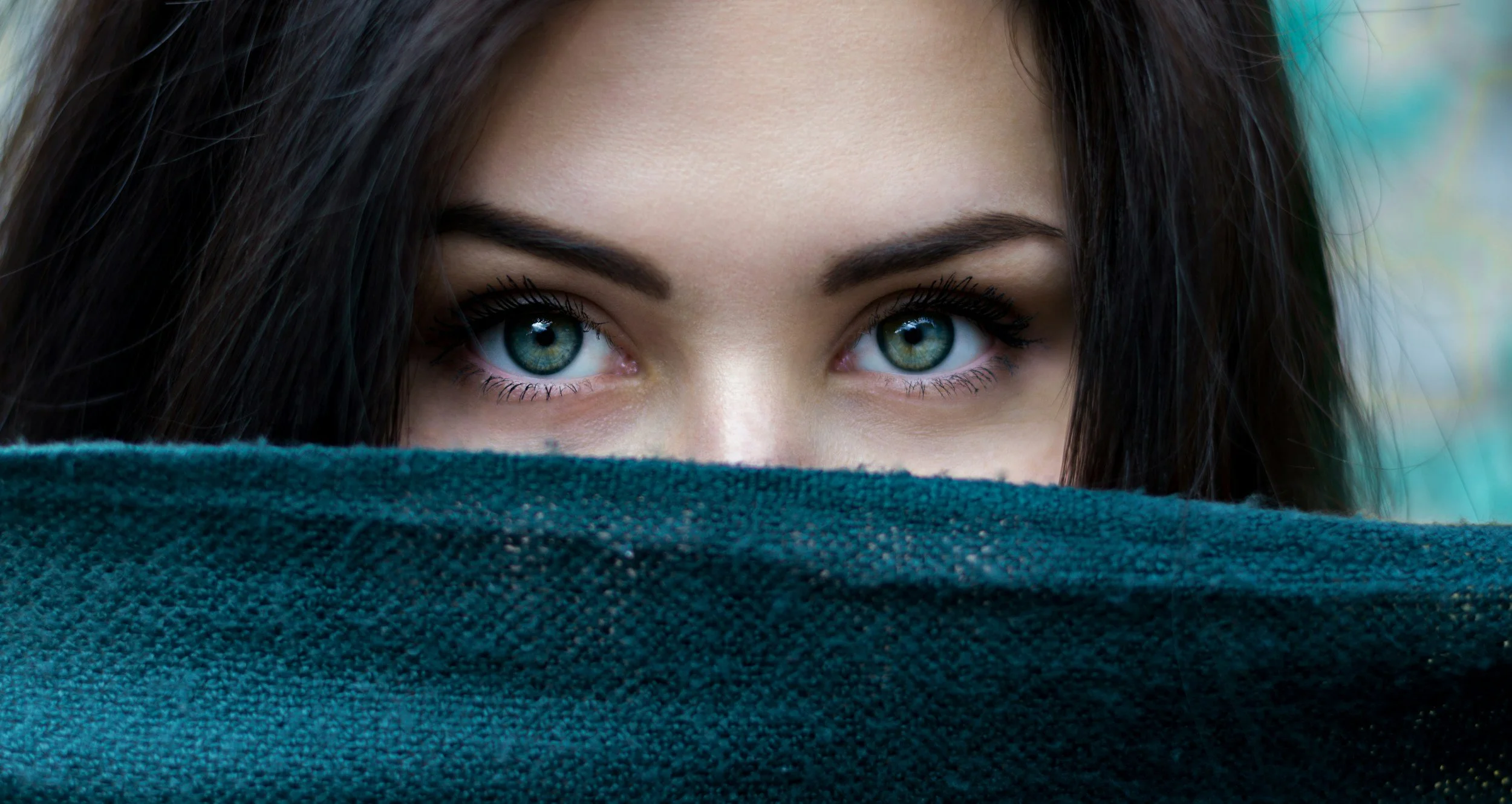 Close-up of a woman's face with piercing blue eyes, partly hidden behind a teal cloth.  She is receiving personalized guidance to banish period pain