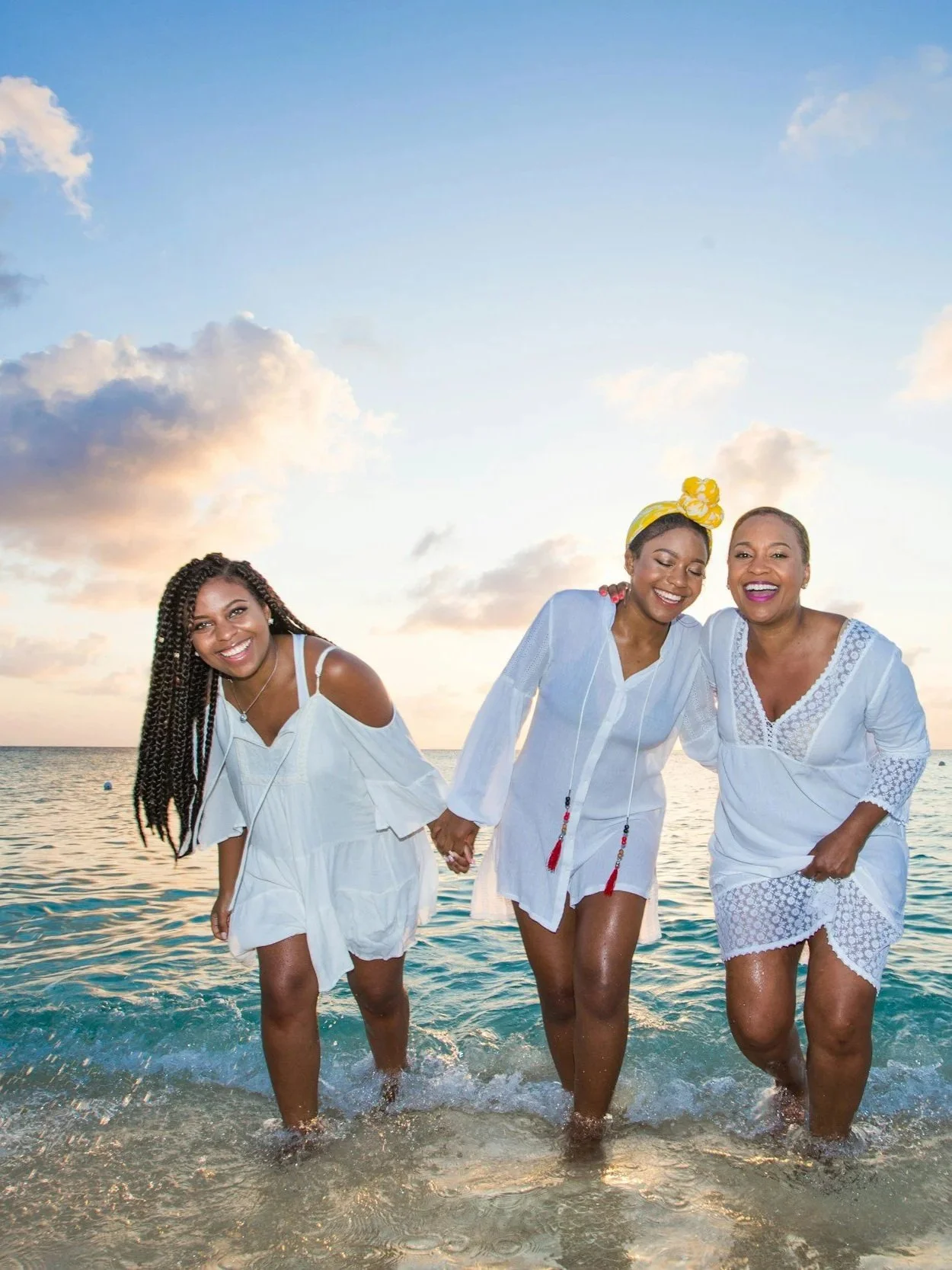 Three women in white dresses walking hand in hand along the shoreline at sunset, they are happy and confident because they have reproductive freedom.