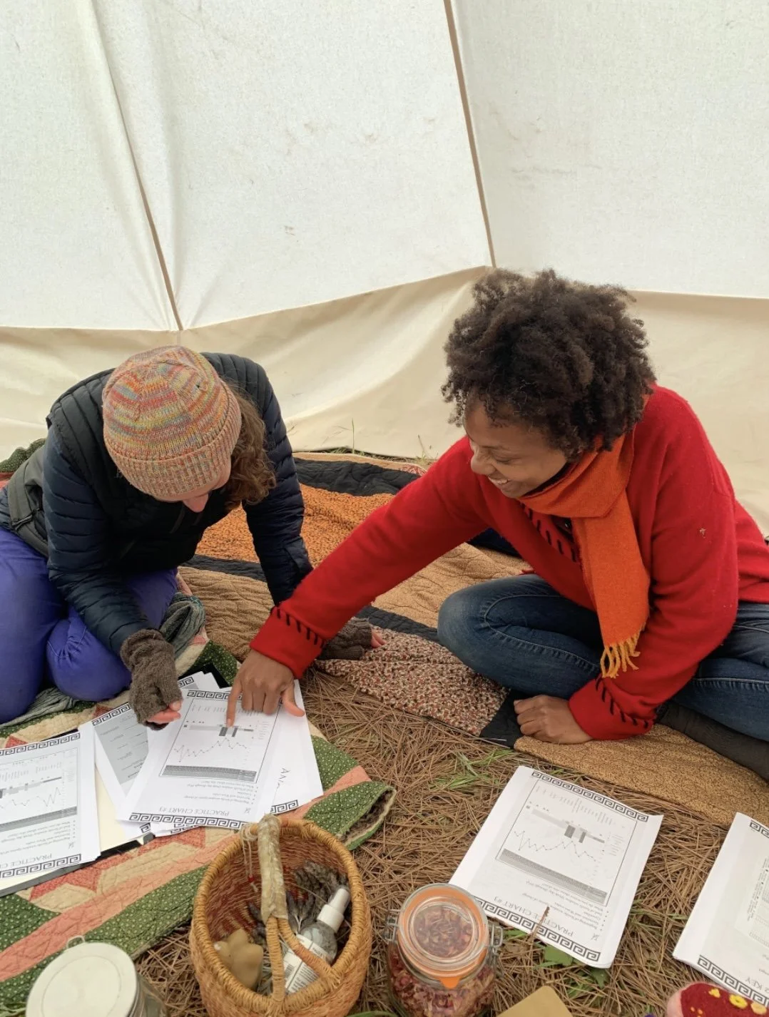Two women sitting on the ground, reviewing and discussing documents with graphs and charts, they are in a fertility awareness and natural birth control course.