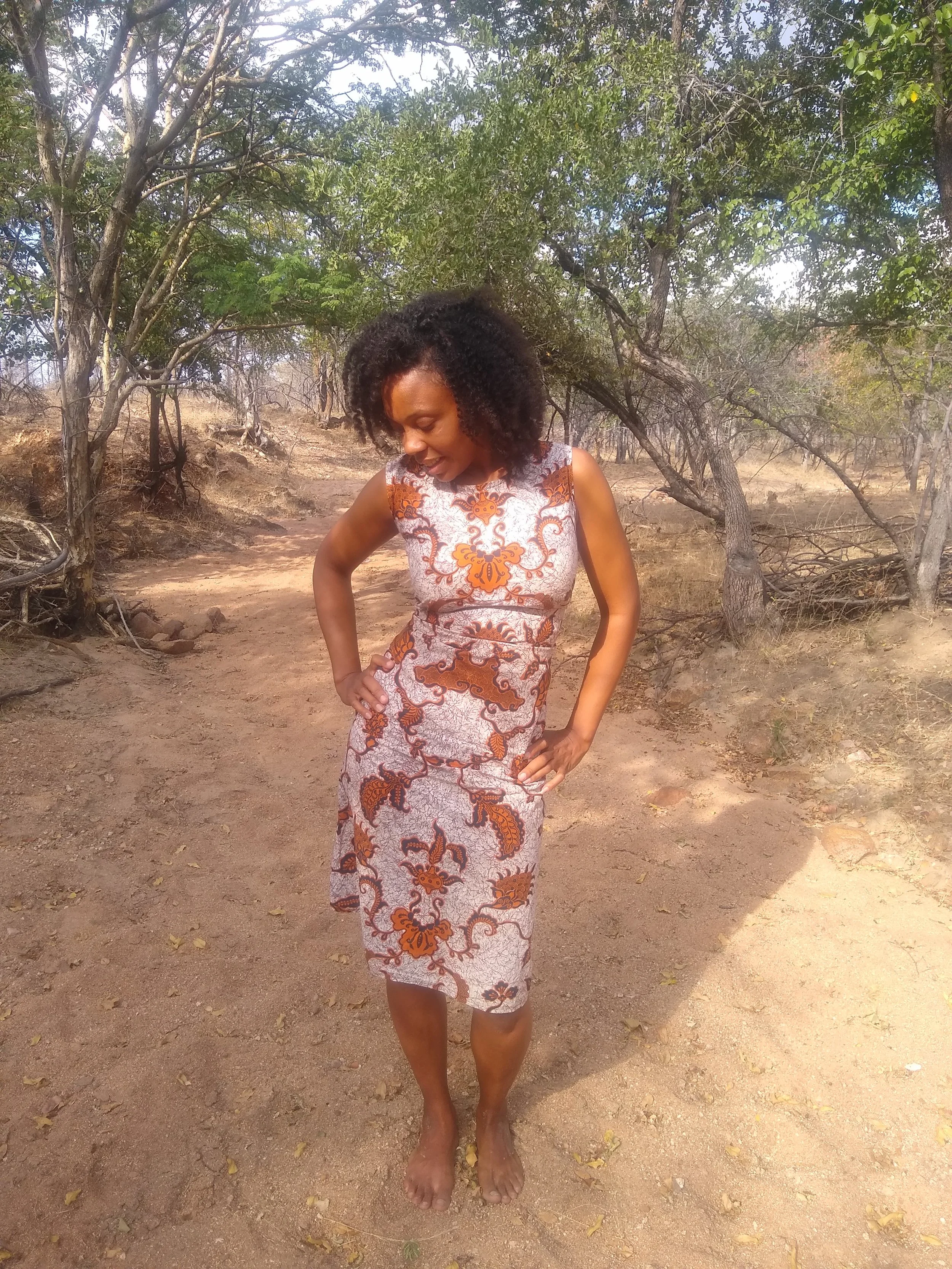 Woman with curly hair looking down, standing outdoors on dirt ground surrounded by trees, she is empowered to use birth control without hormones with confidence.