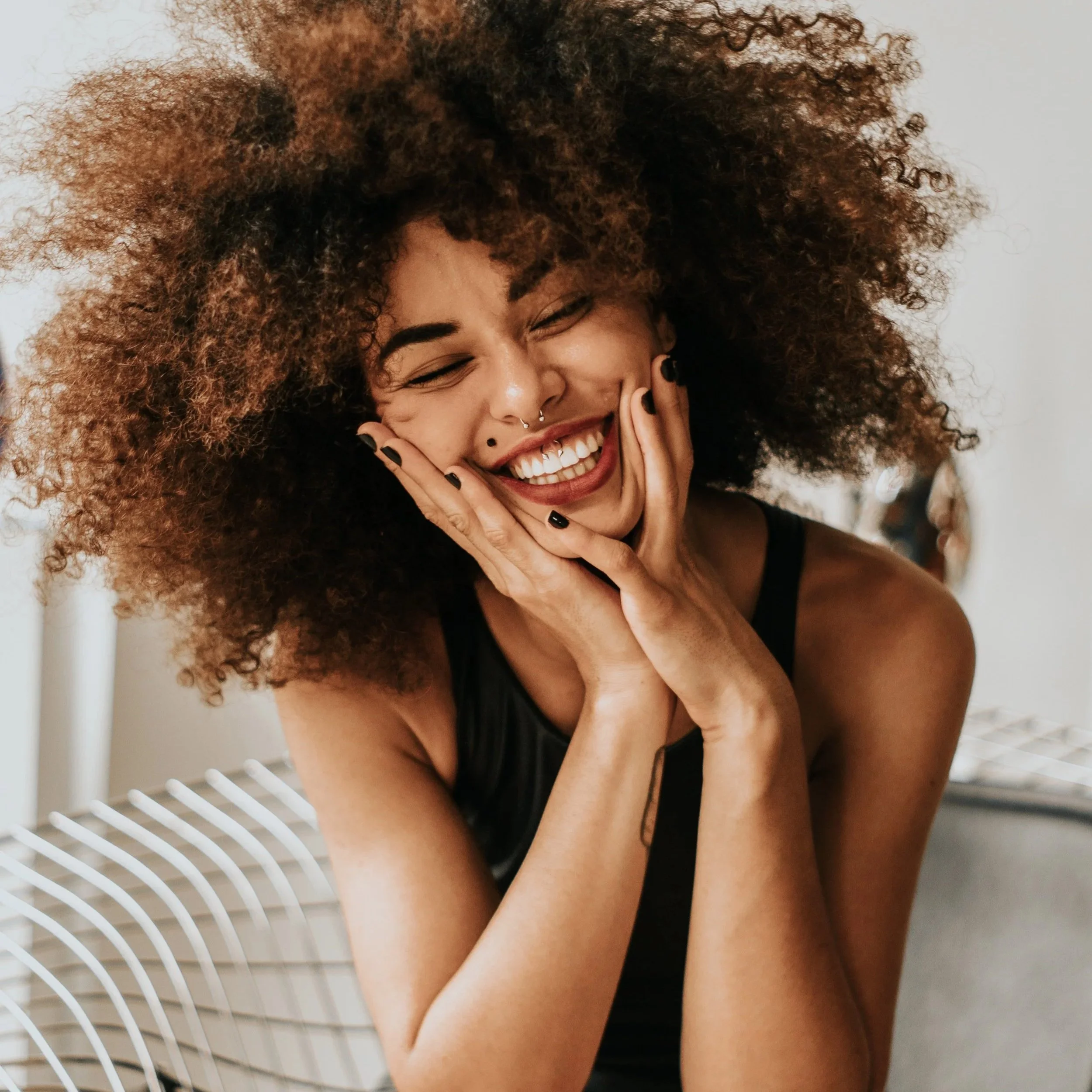 A woman with curly brown hair laughing and touching her face with both hands, she is so excited to use natural birth control that actually works.