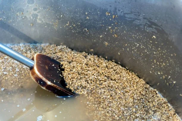 A black scoop stirring a mixture of sand and water in a large container.