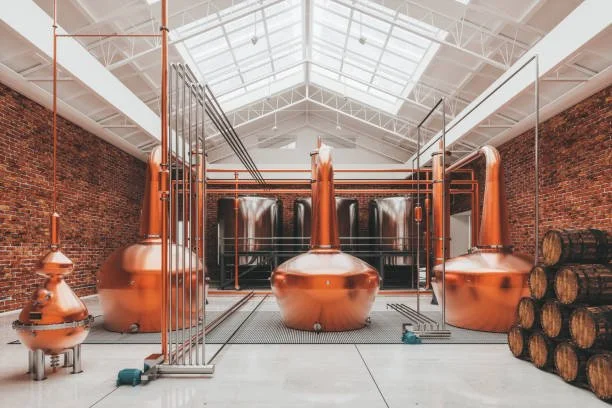 Copper stills used for distillation inside a large industrial space with a glass roof.