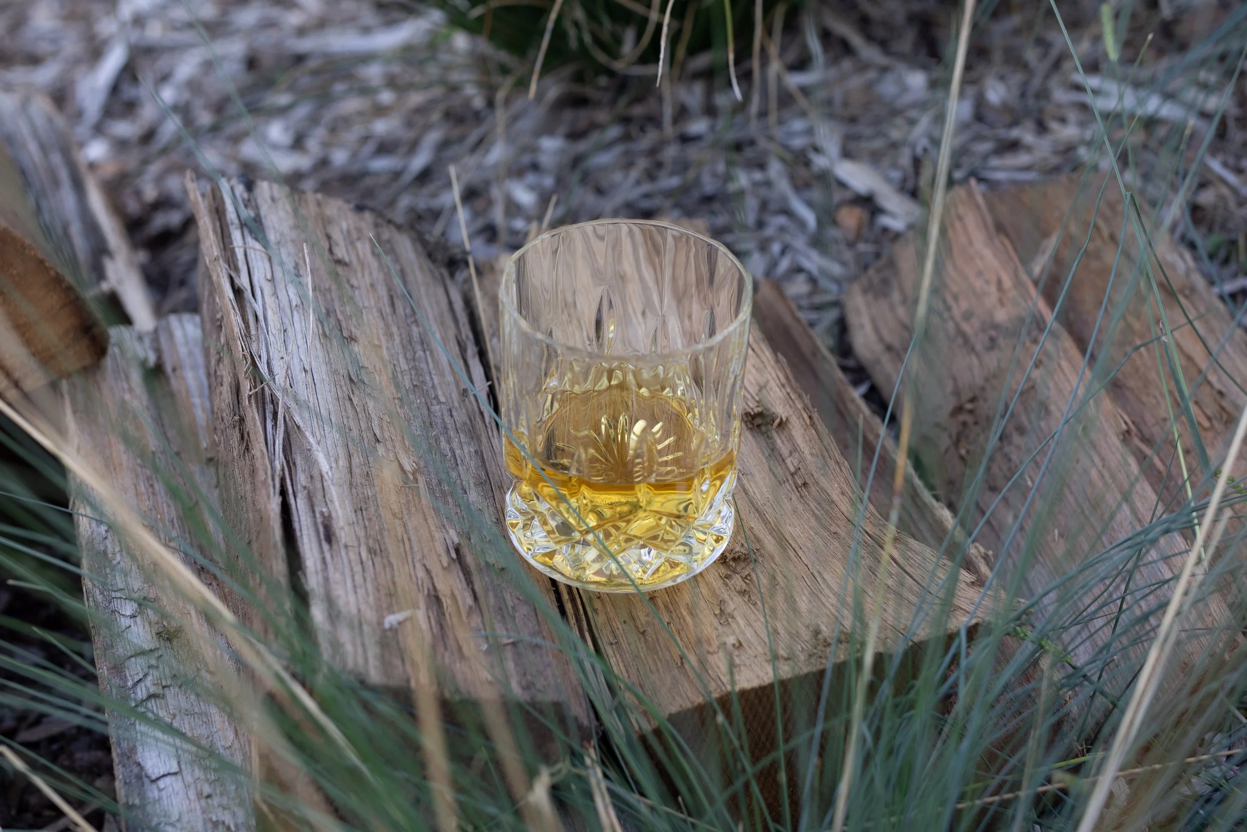 A glass of whisky sitting on firewood logs.