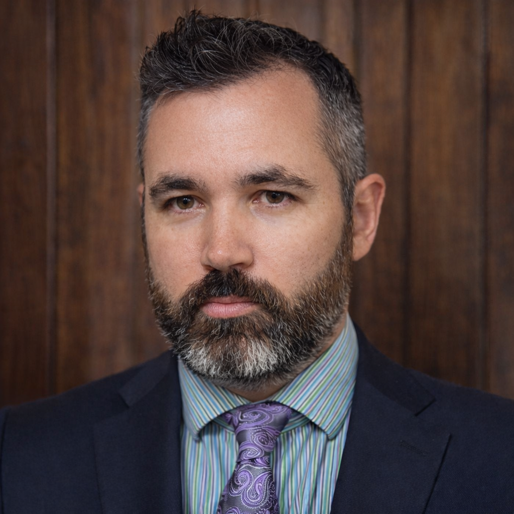 Headshot attorney Jeffrey D. Anson in dark suit and purple tie, facing camera against wood-paneled background