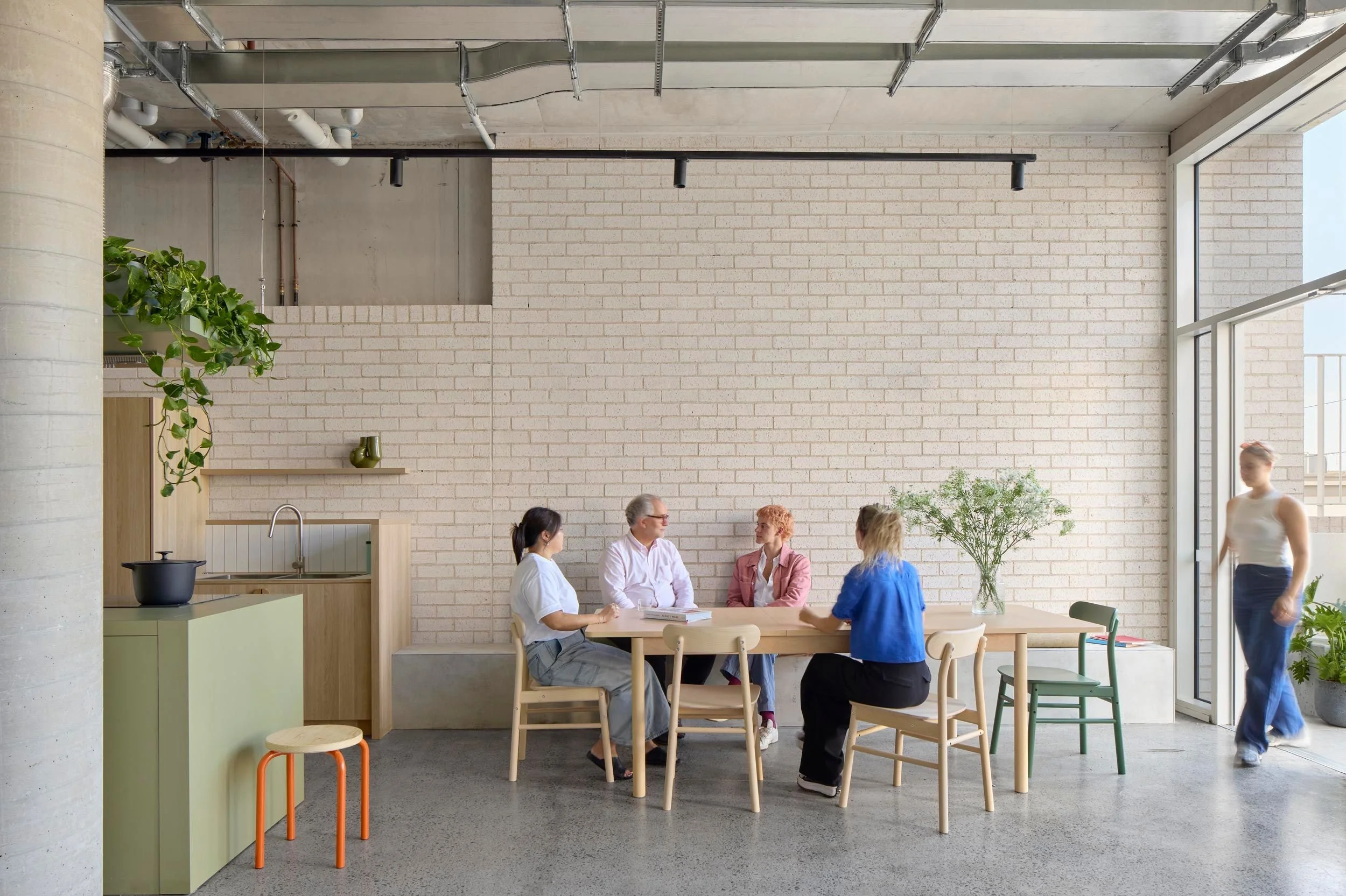 Communal dining area next to communal kitchen. Four people are seated and talking at a large table.
