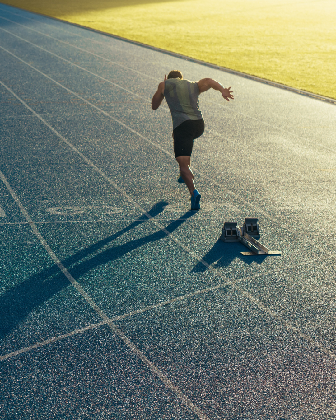 Male sprinter starting a race on a track, with starting blocks nearby, during sunrise or sunset.